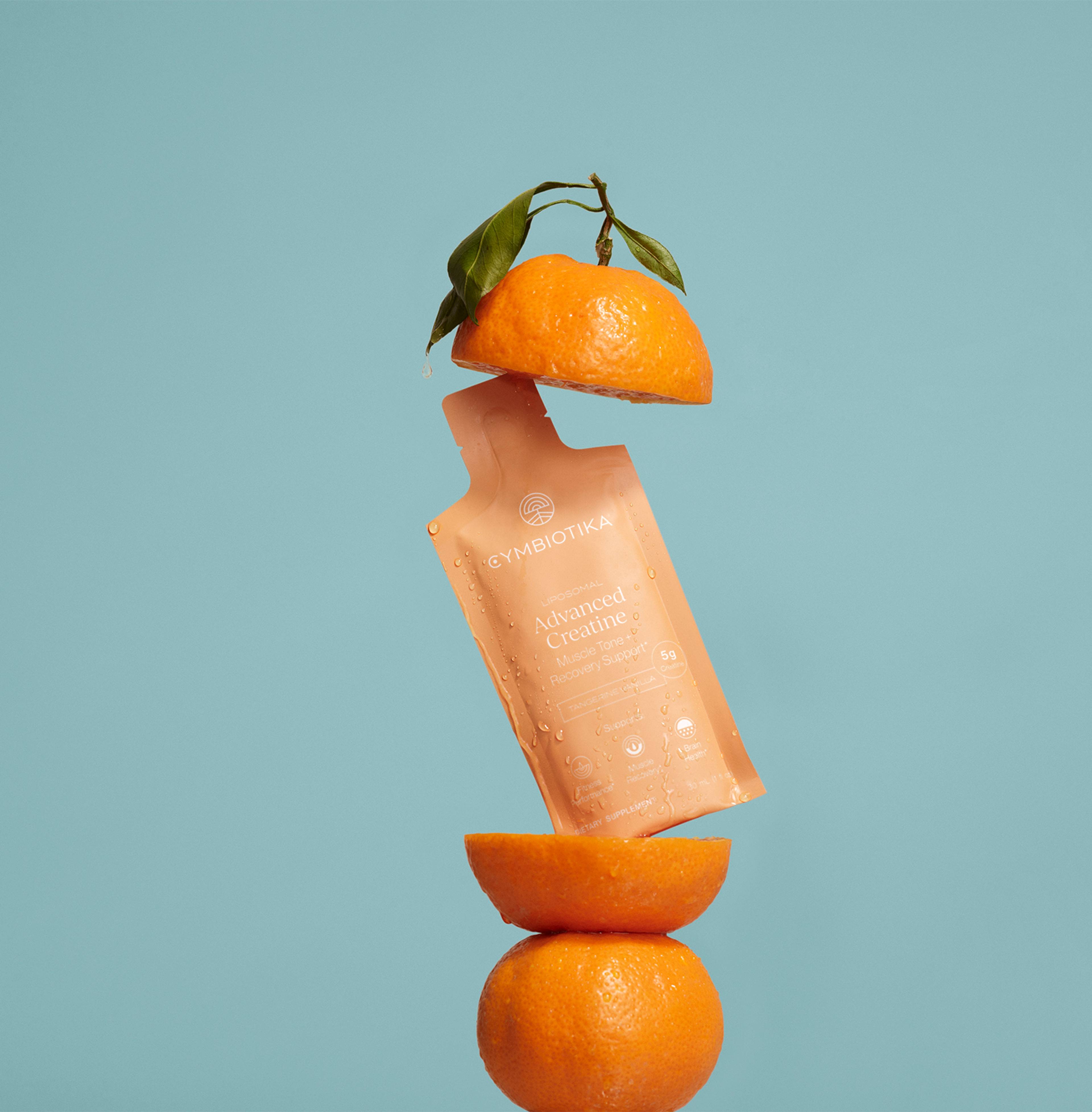 Orange Advanced Creatine sachet suspended between orange halves against a blue background.