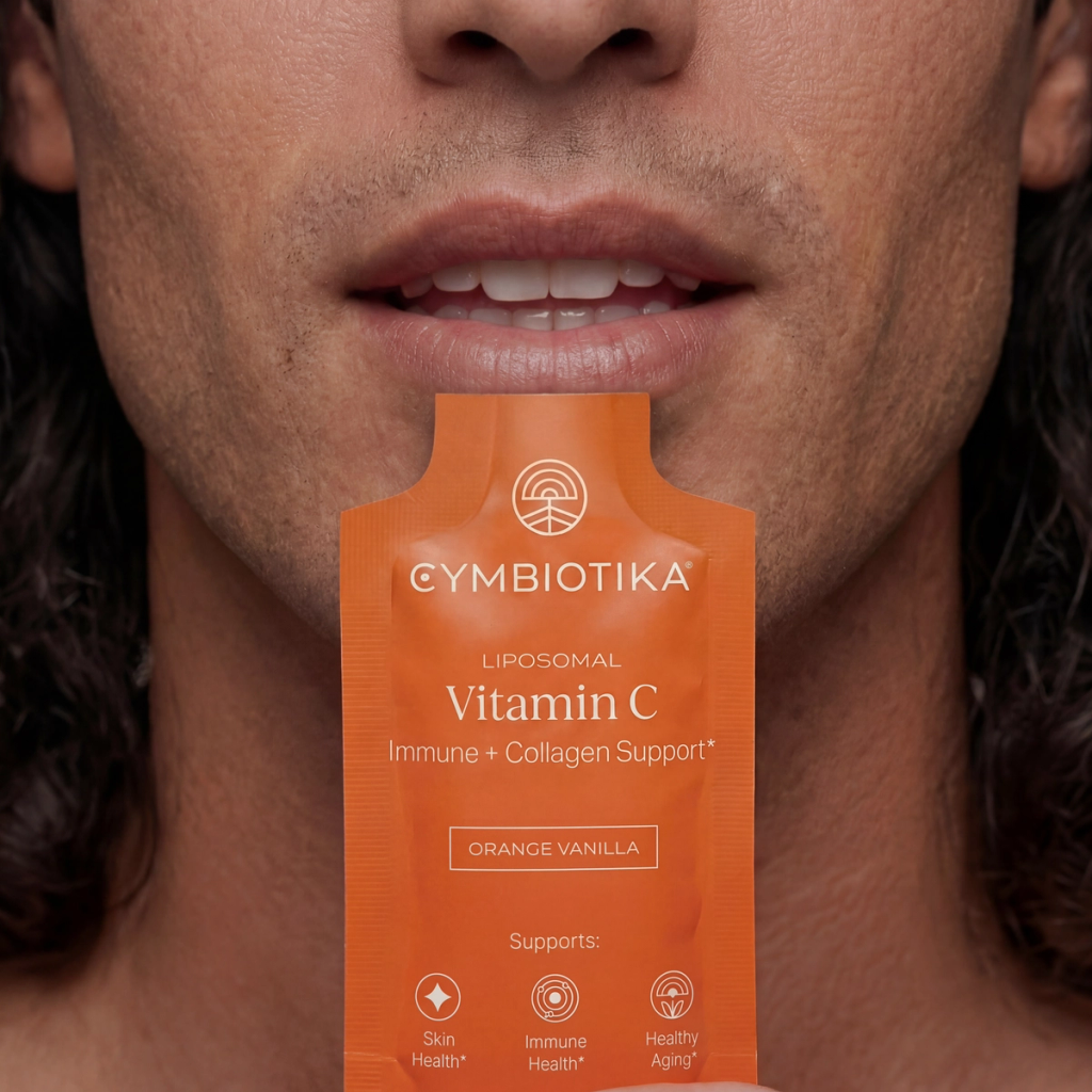 Person holds an orange Cymbiotika Liposomal Vitamin C packet below their mouth, showing its Orange Vanilla flavor label.