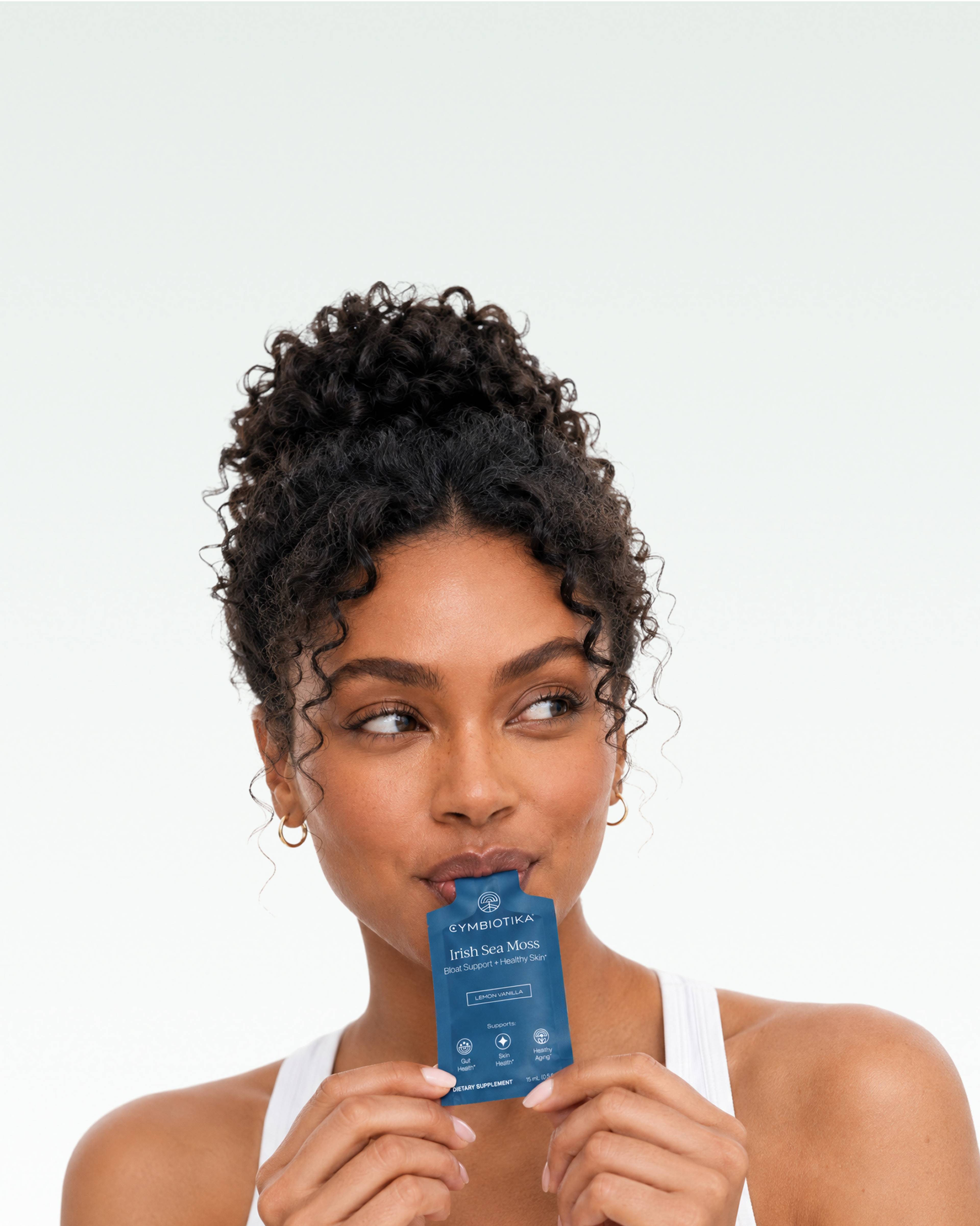Woman holds a blue Cymbiotika Irish Sea Moss sachet to her lips.