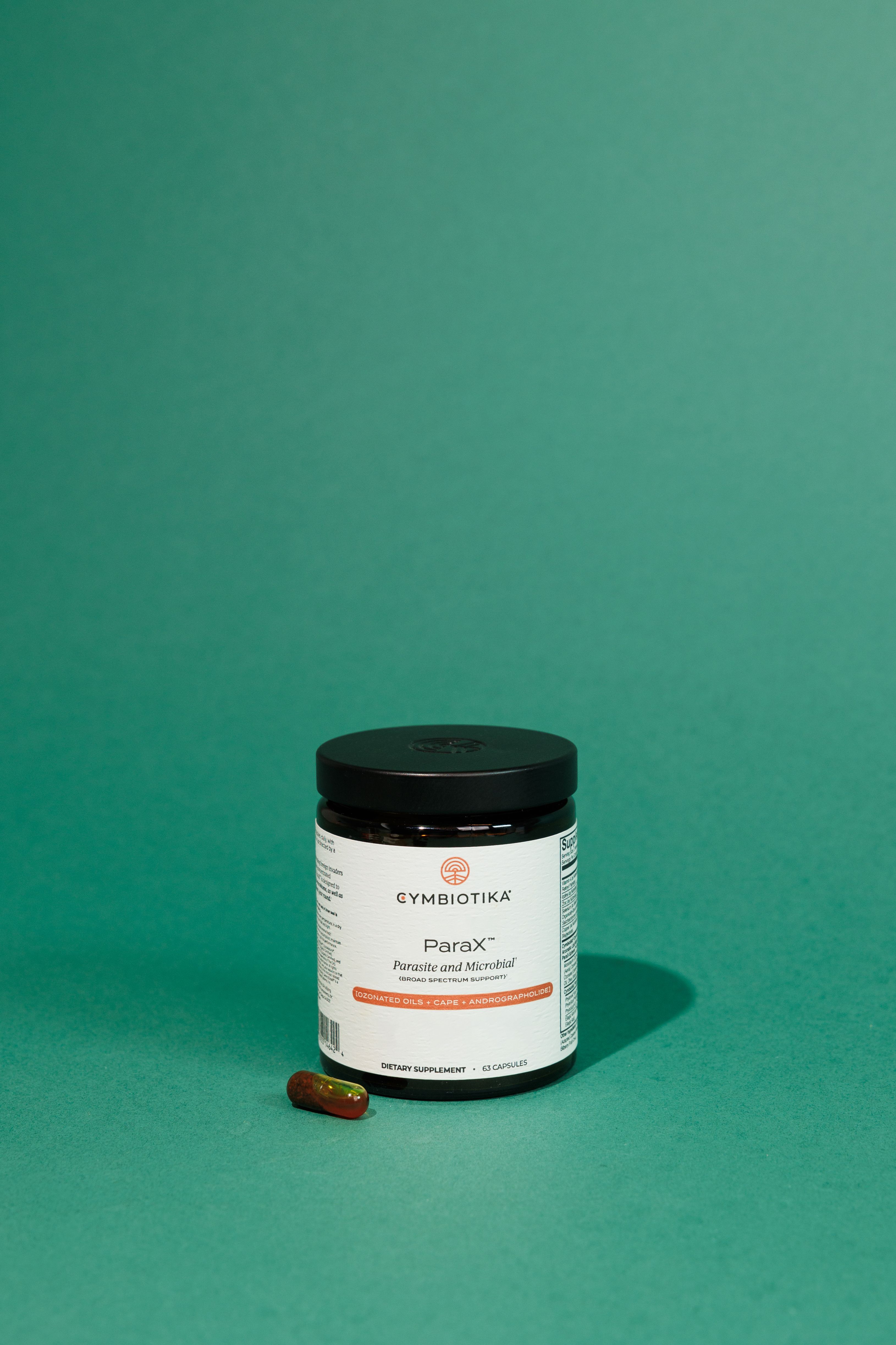 ParaX supplement bottle and a capsule on a teal surface.