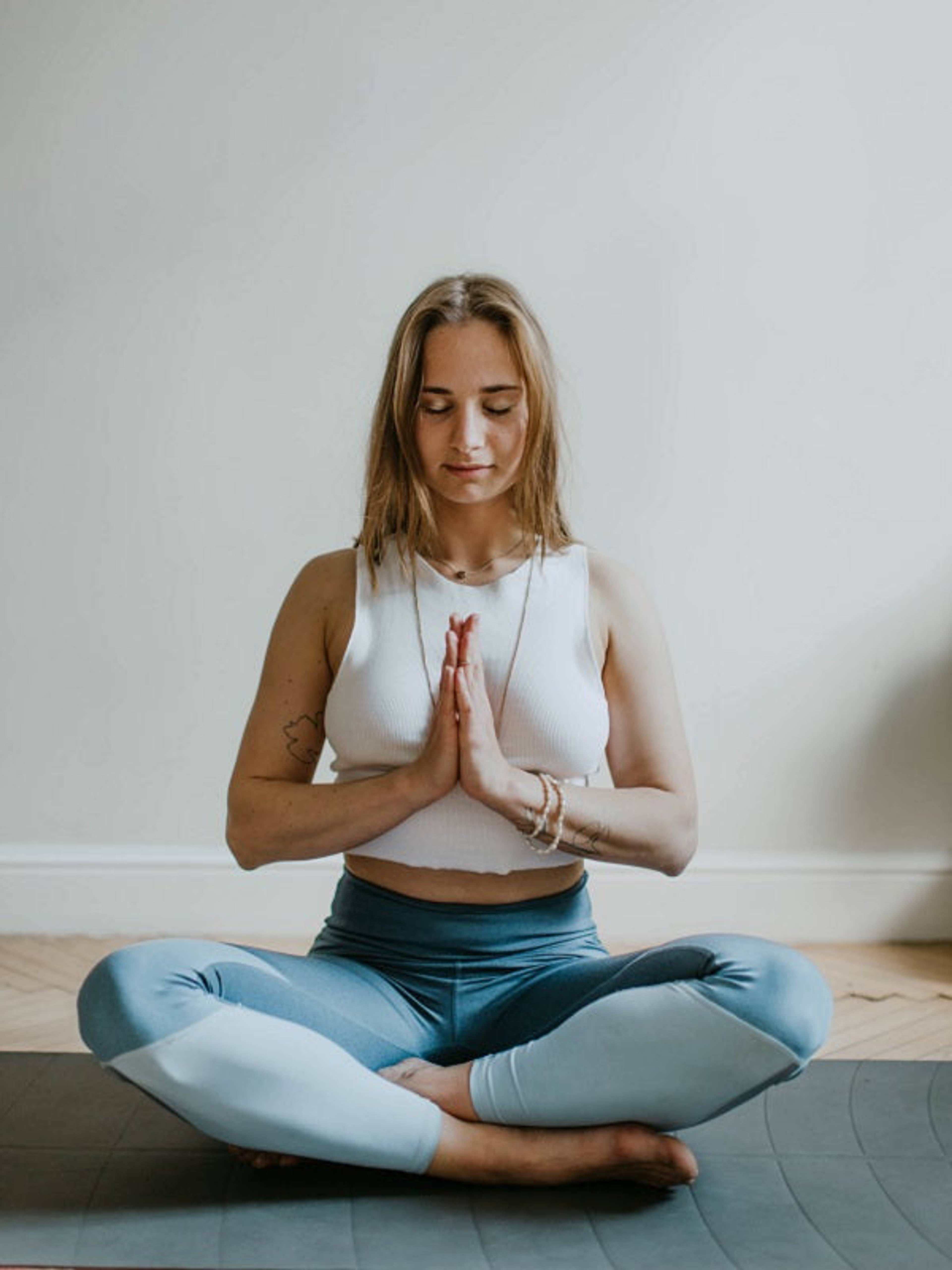 Woman sitting cross-legged on a yoga mat with hands together and eyes closed.