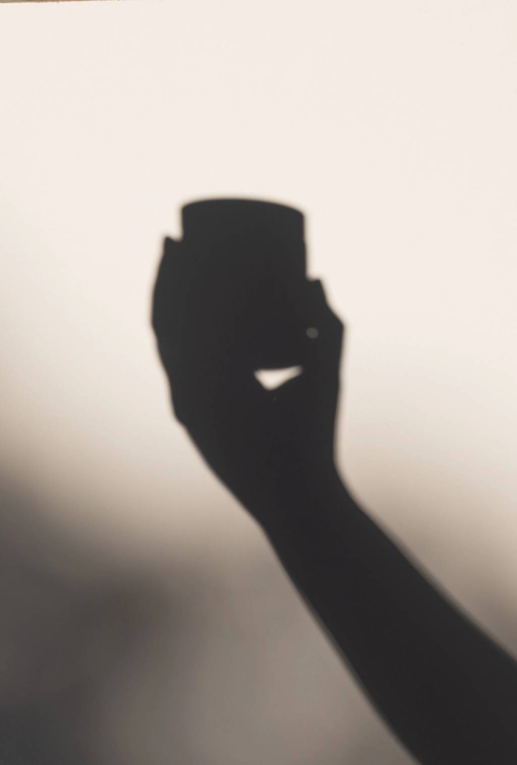 Shadow of a hand holding a small container against a softly lit background.