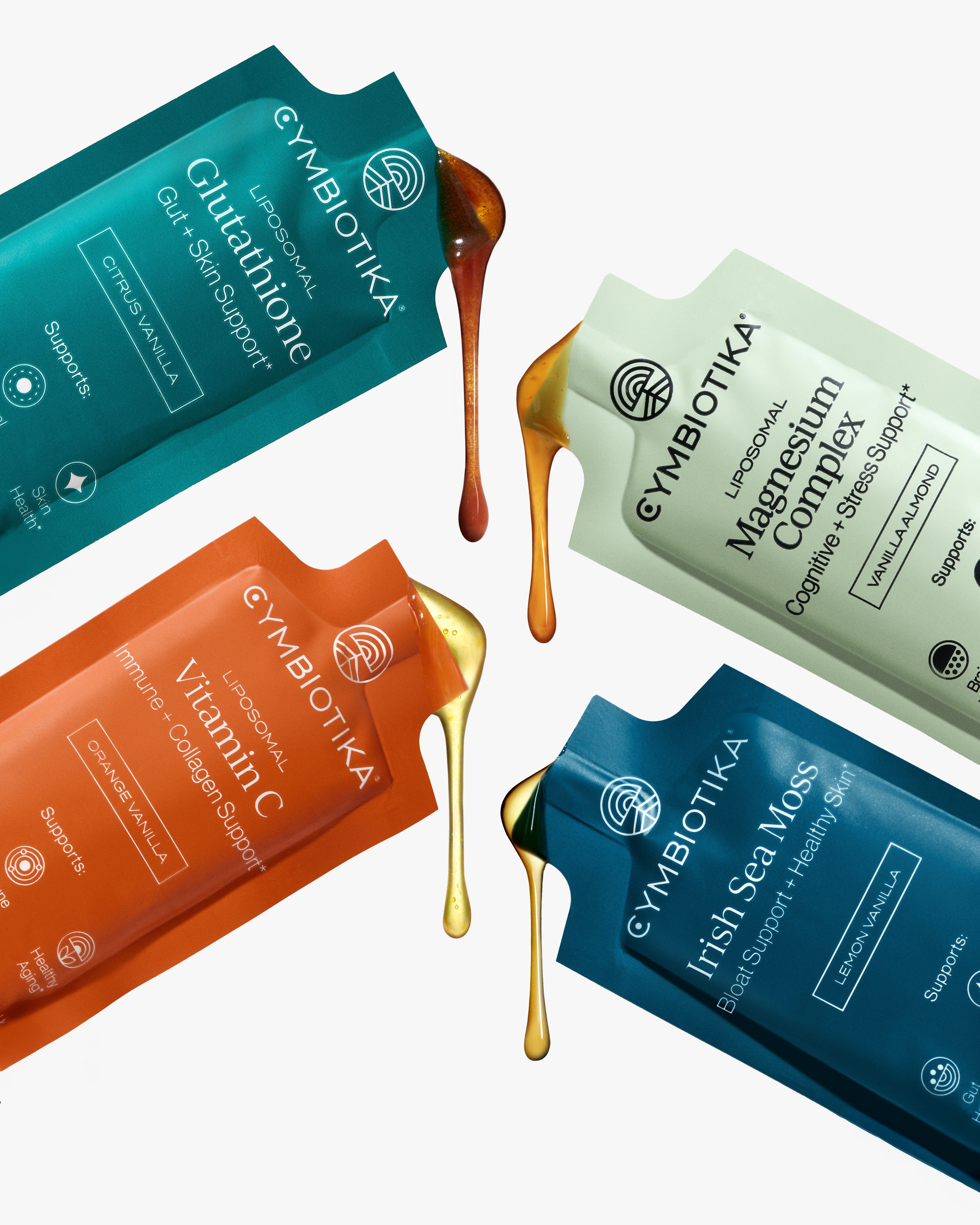 Four Cymbiotika supplement sachets with amber and gold liquid drips on a white background.