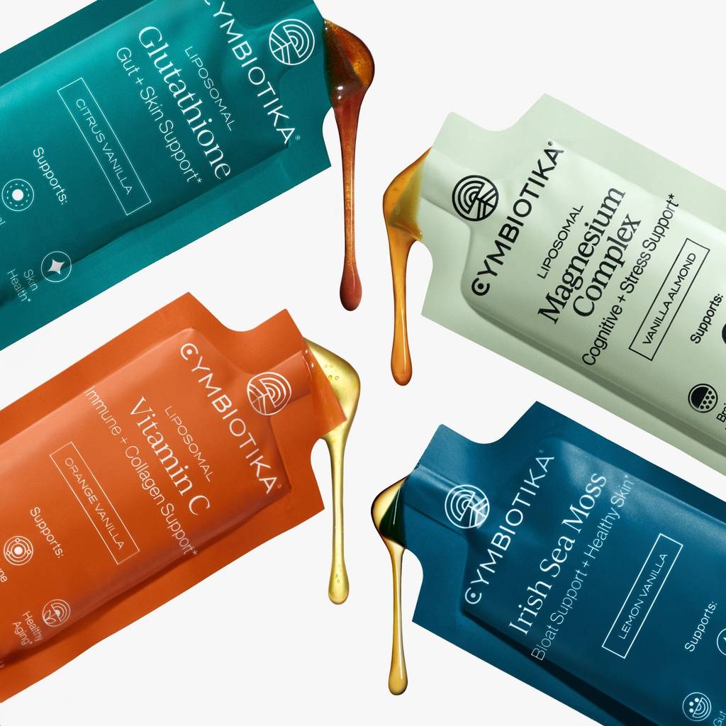 Four Cymbiotika supplement sachets with amber and gold liquid drips on a white background.