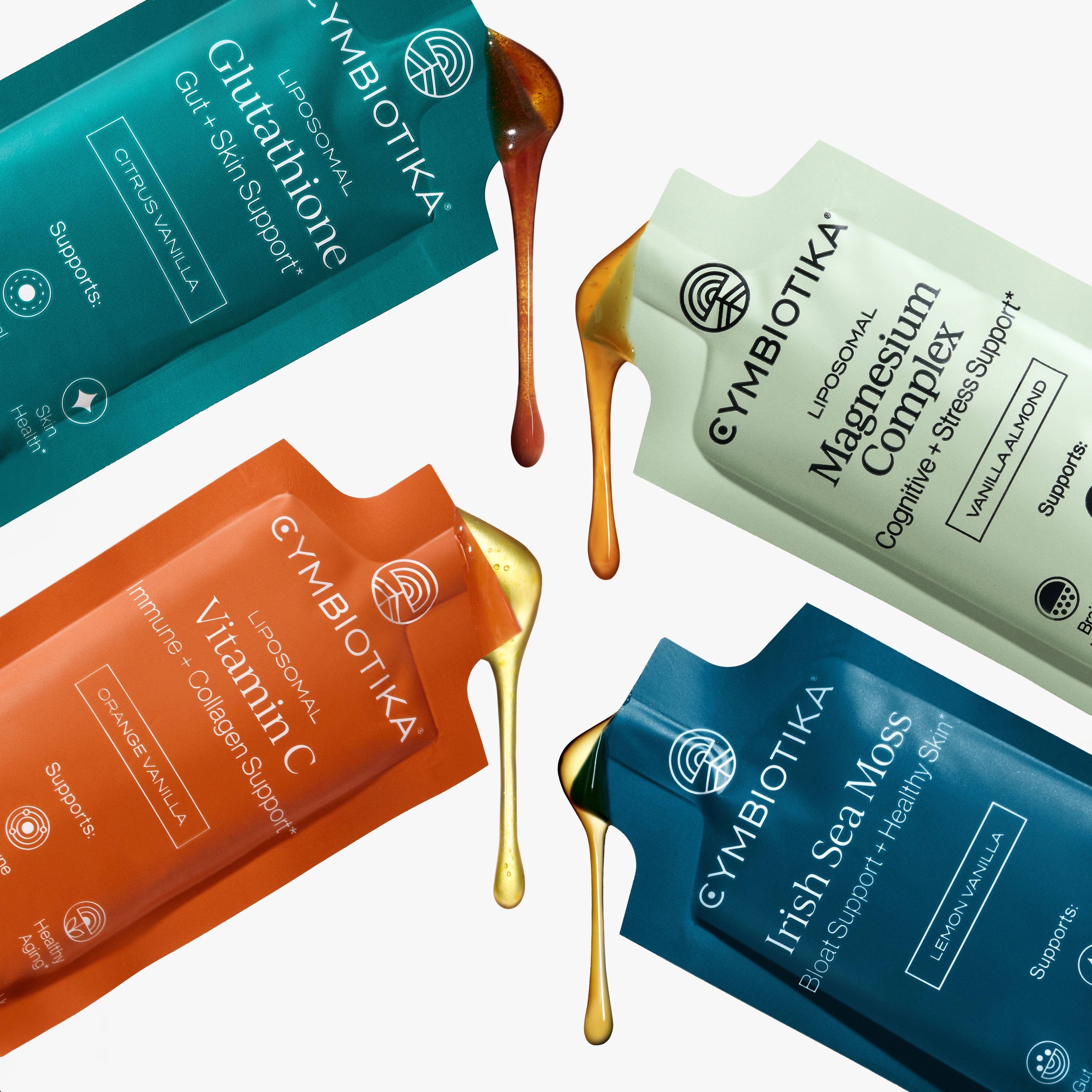 Four Cymbiotika supplement sachets with amber and gold liquid drips on a white background.