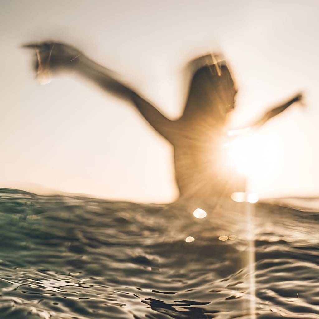 Blurred person with arms raised standing in ocean water at sunset.