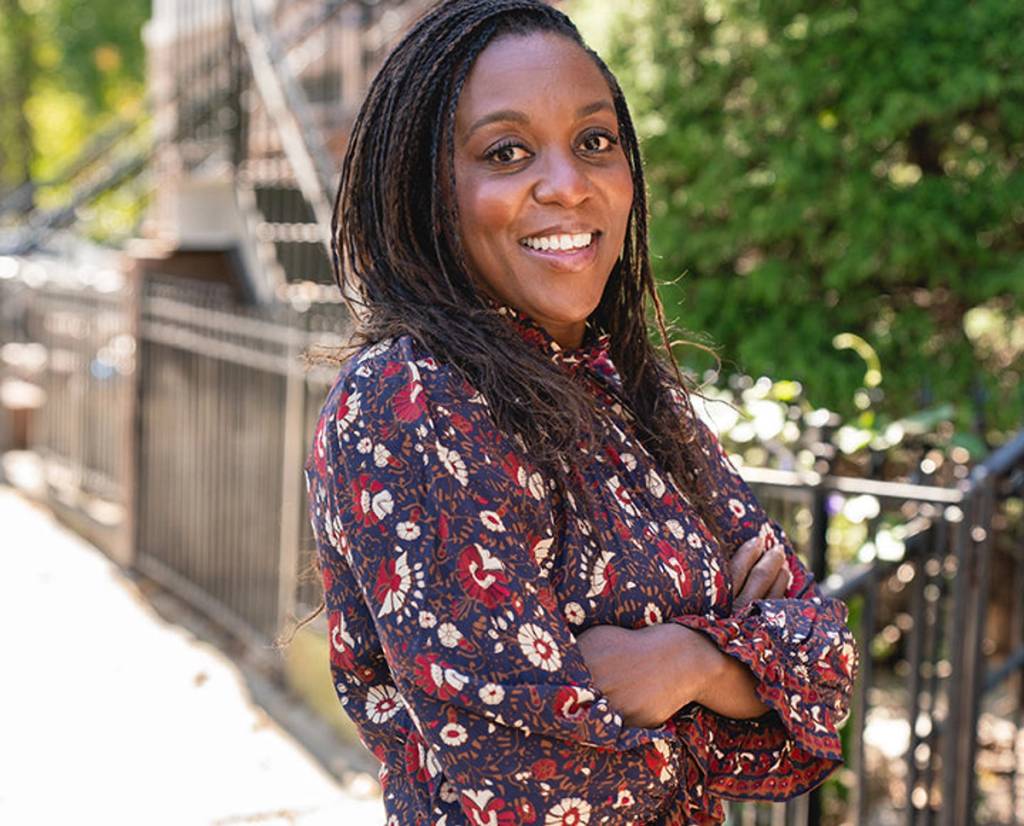 Smiling woman in a floral blouse standing outdoors with her arms crossed.