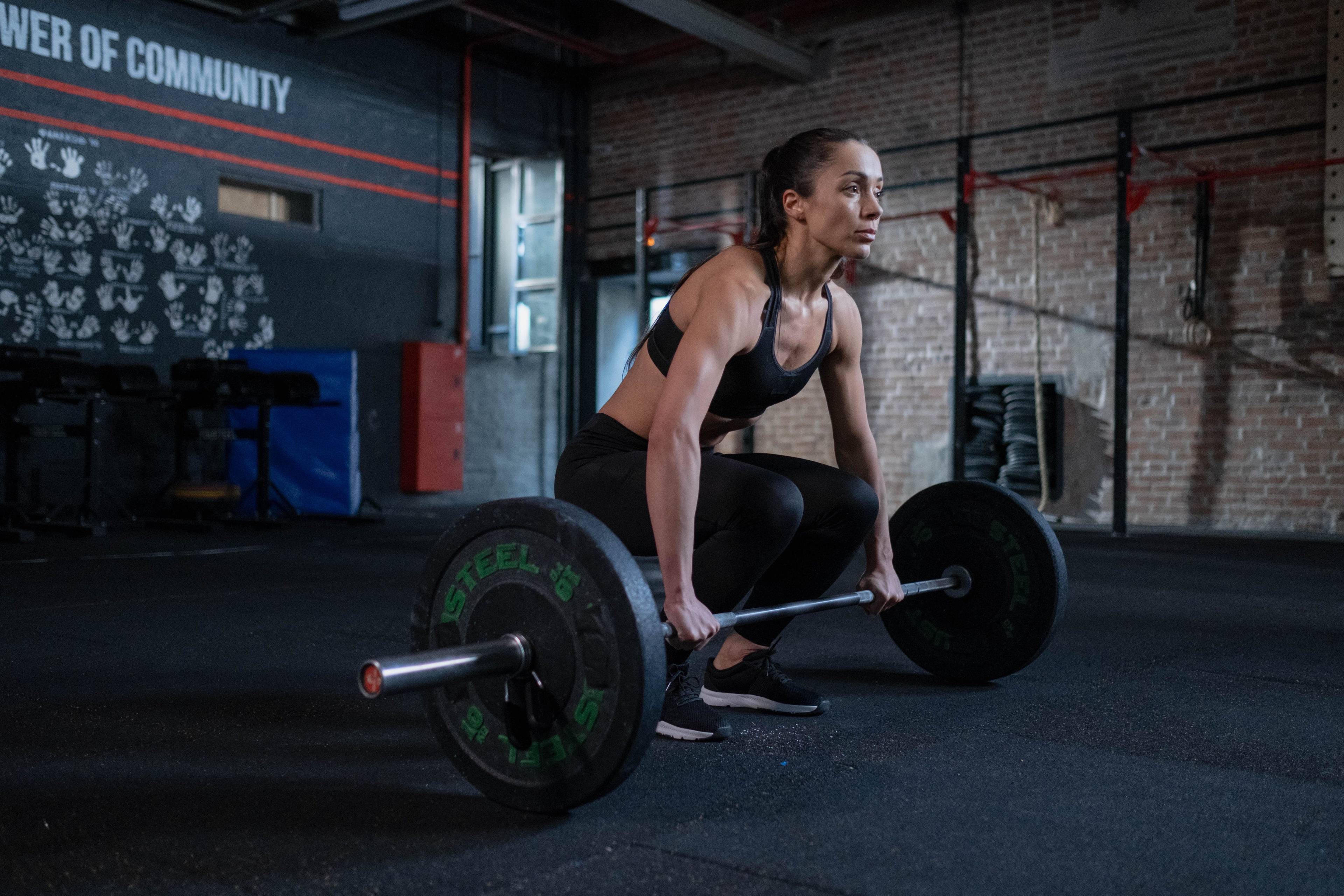 Woman in black workout clothes preparing to lift a loaded barbell in a gym.