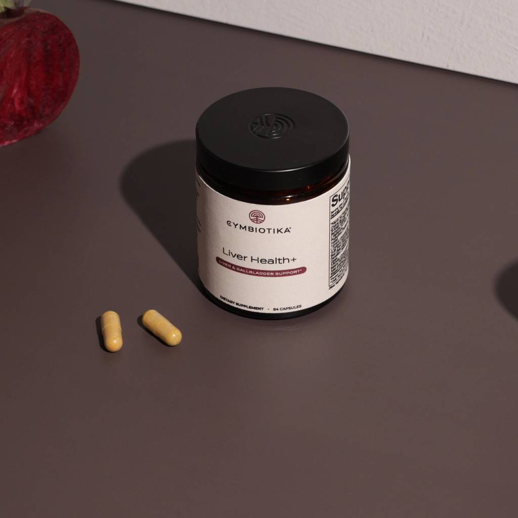 Cymbiotika Liver Health+ jar with two capsules on a dark tabletop beside beets