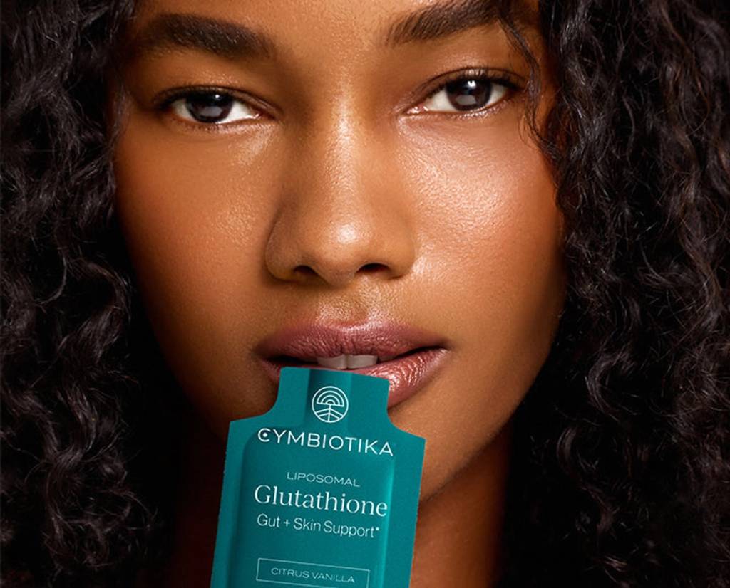 Woman holding a Cymbiotika Liposomal Glutathione packet between her lips.