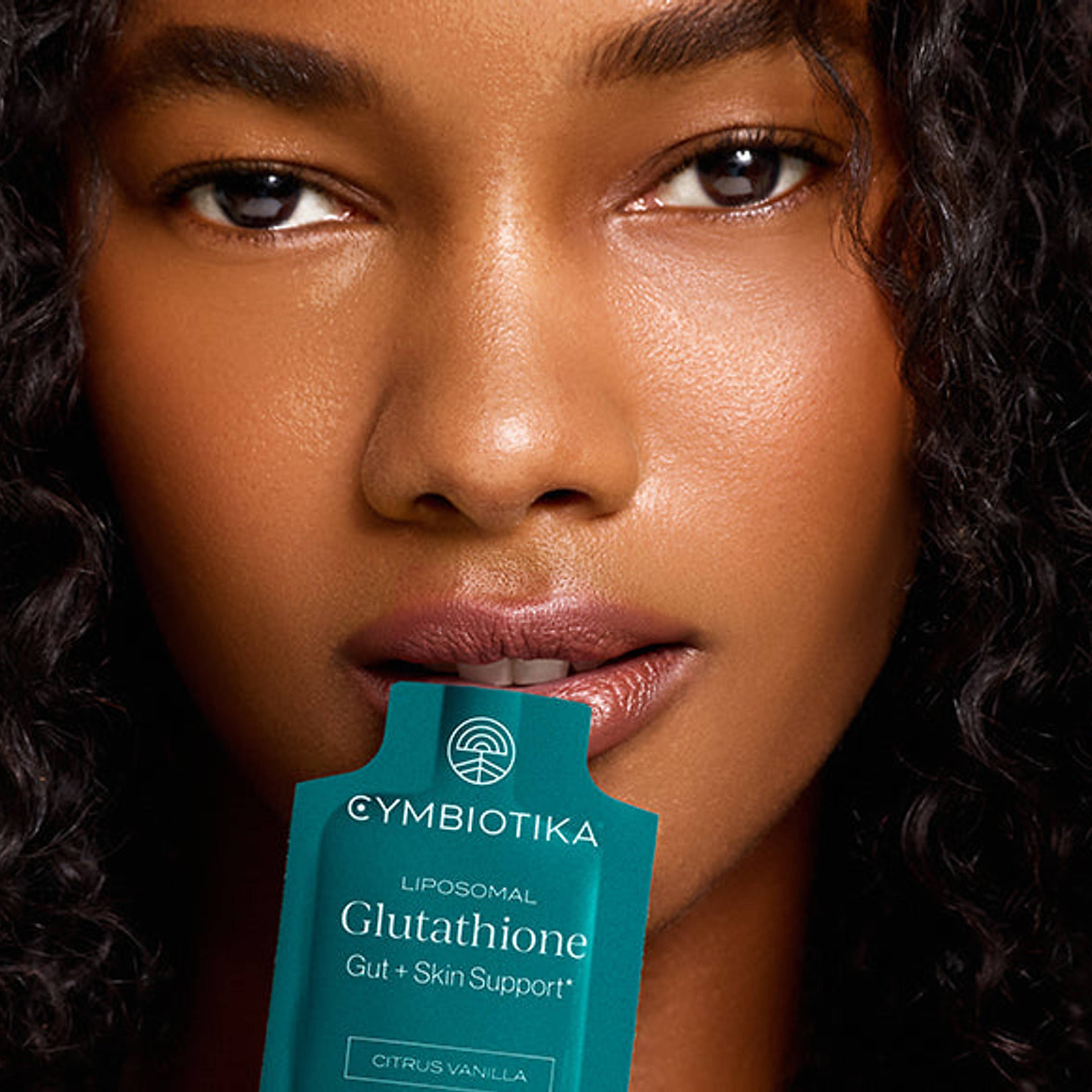 Woman holding a Cymbiotika Liposomal Glutathione packet between her lips.