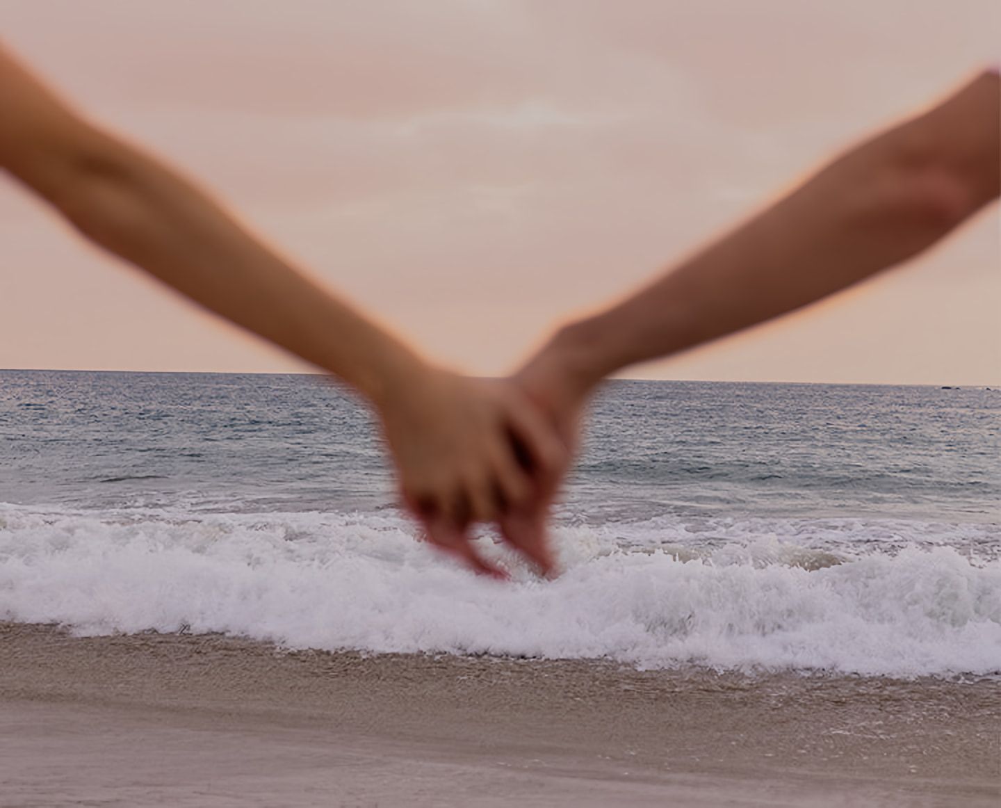 Two hands clasped above breaking waves on a beach.
