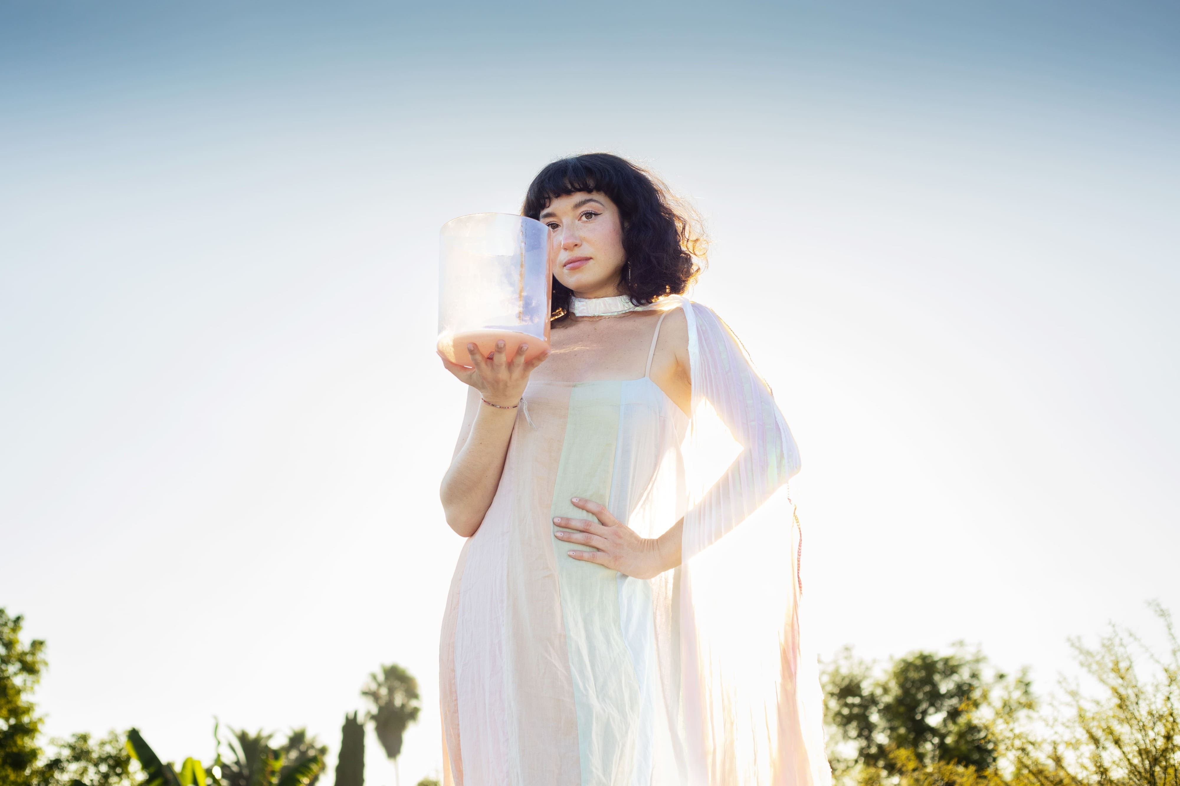 Woman in a light sheer dress holding a pale translucent cylindrical object outdoors.