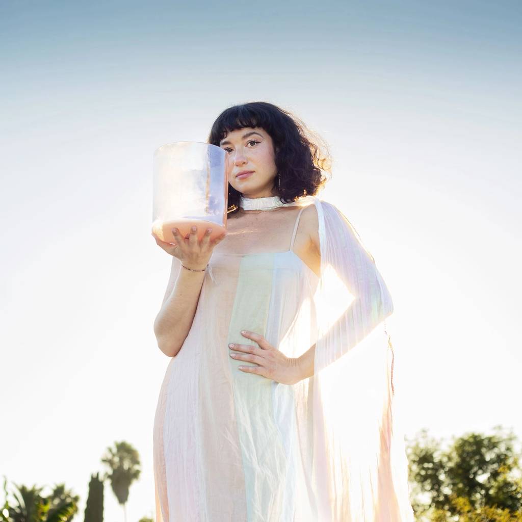 Woman in a light sheer dress holding a pale translucent cylindrical object outdoors.