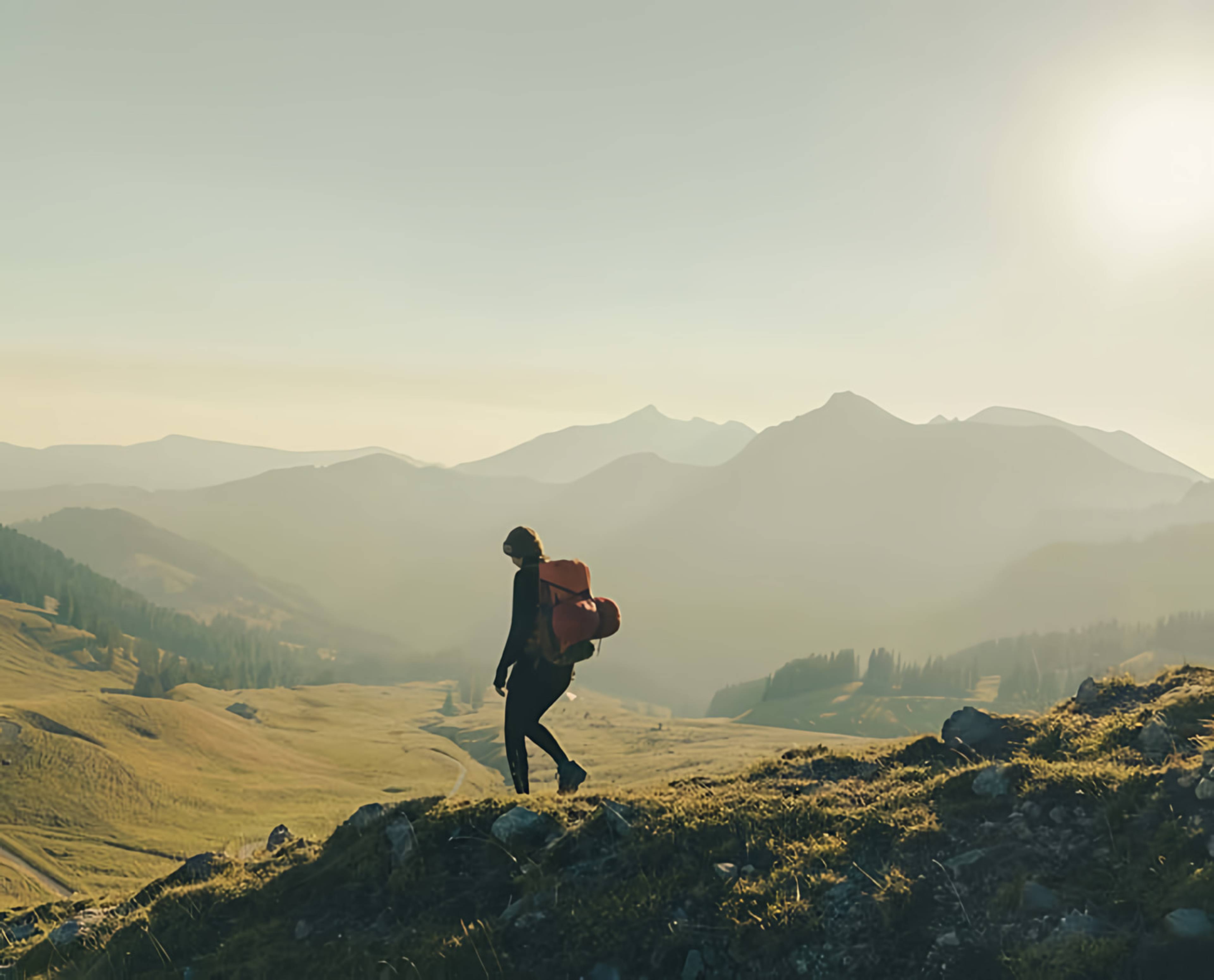 Hiker with a backpack walking along a rocky mountain ridge in warm low sunlight.