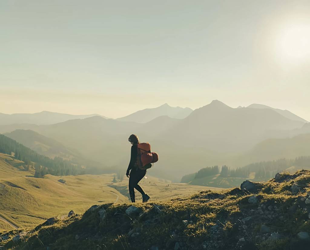 Hiker with a backpack walking along a rocky mountain ridge in warm low sunlight.