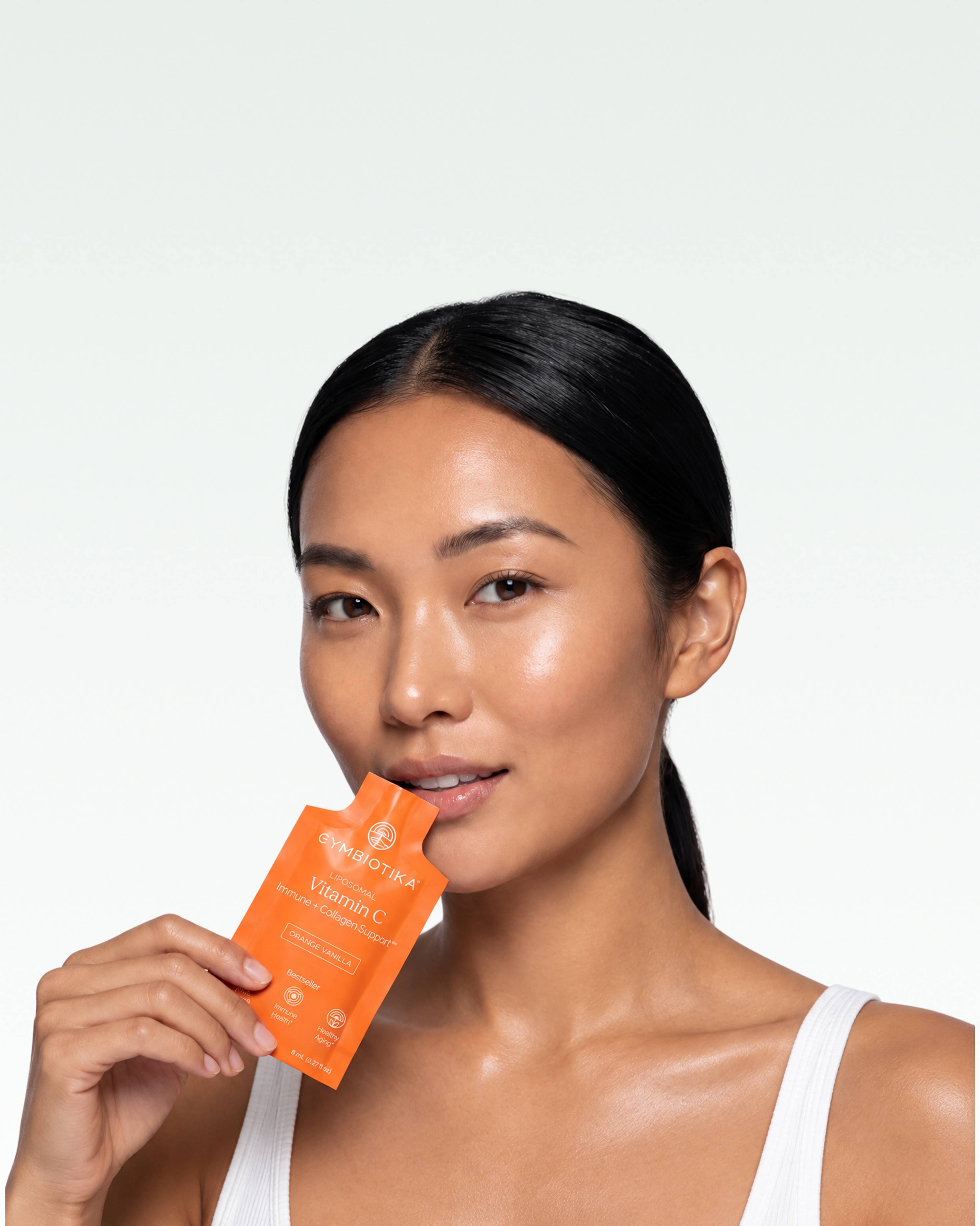 Woman holding an orange Cymbiotika Vitamin C sachet near her lips.