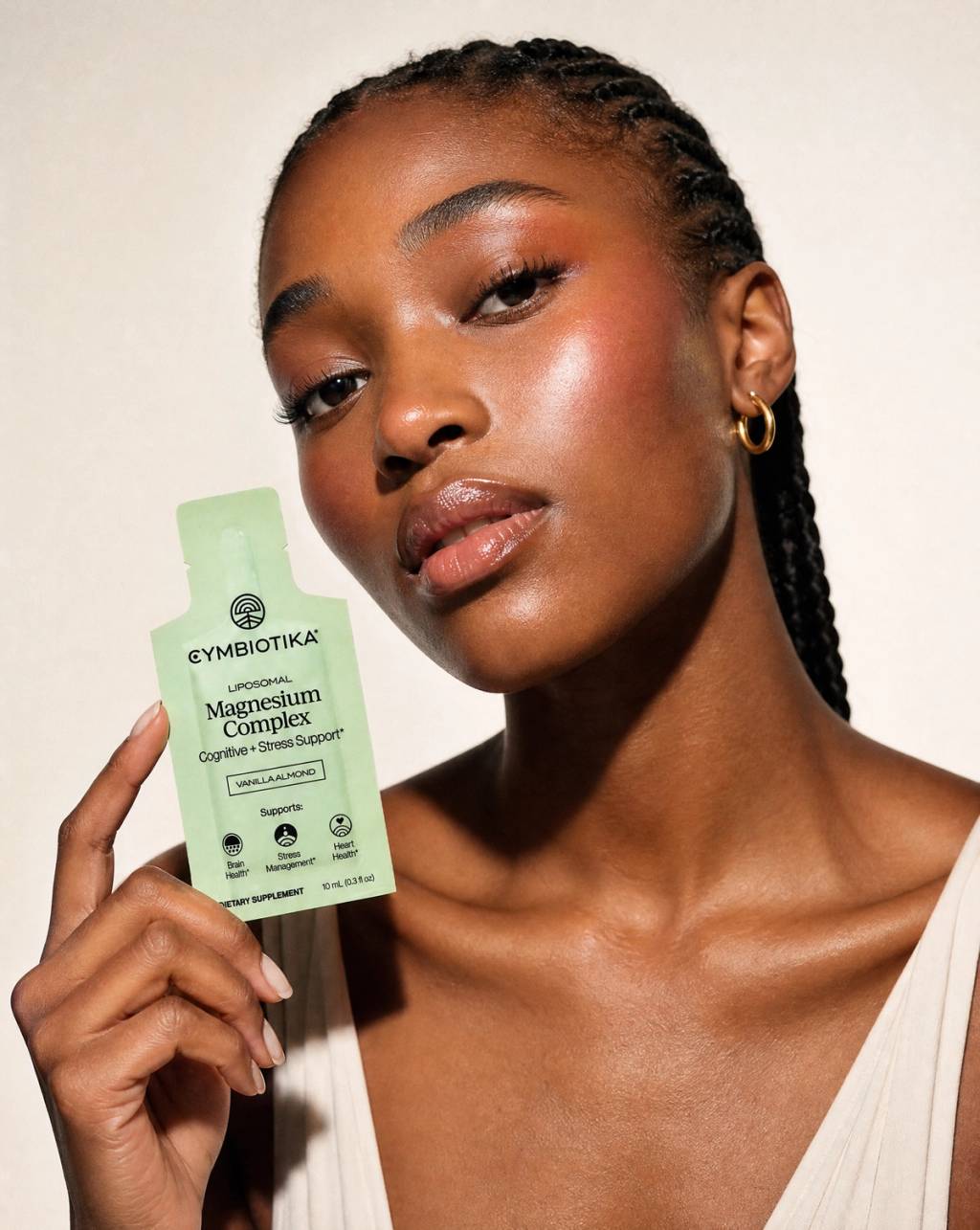 Woman holding a Cymbiotika Liposomal Magnesium Complex packet beside her face.