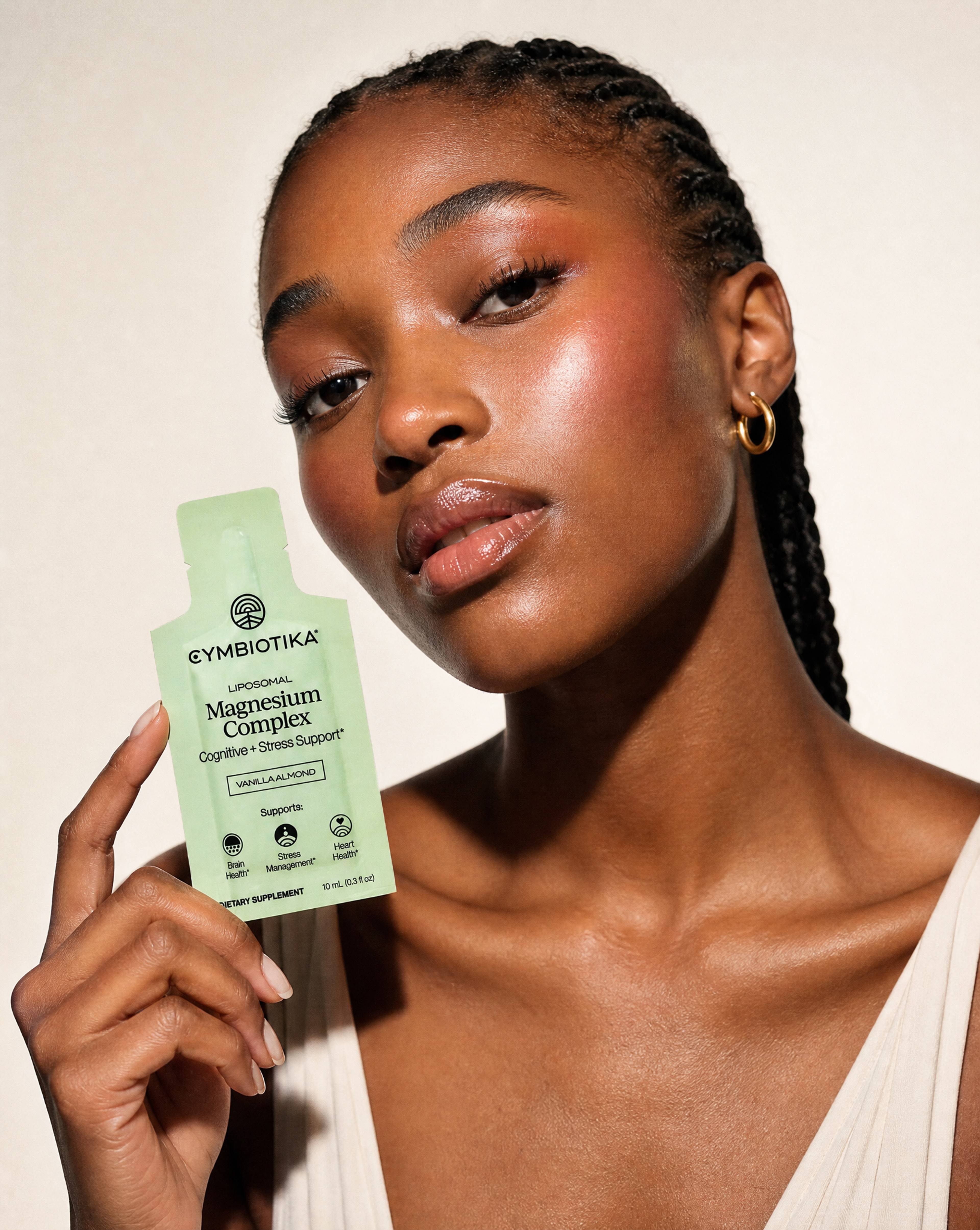 Woman holding a Cymbiotika Liposomal Magnesium Complex packet beside her face.