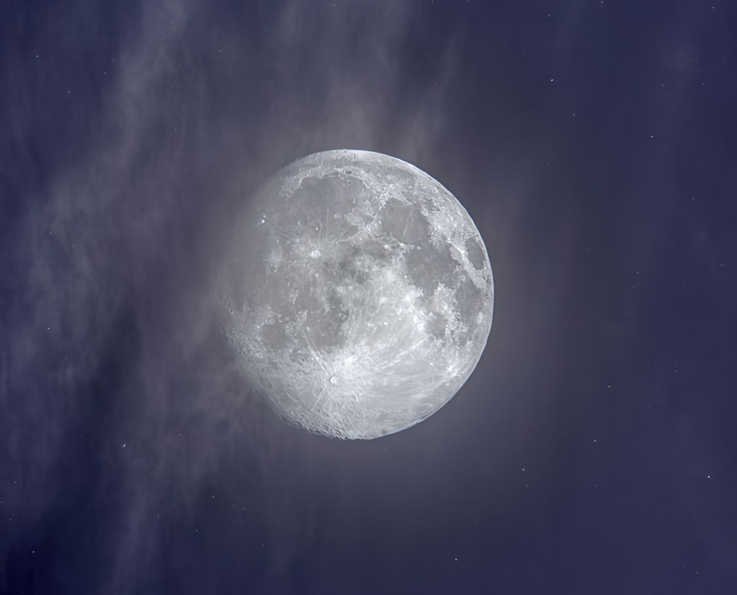 Bright full moon amid wispy clouds in a dark blue night sky.