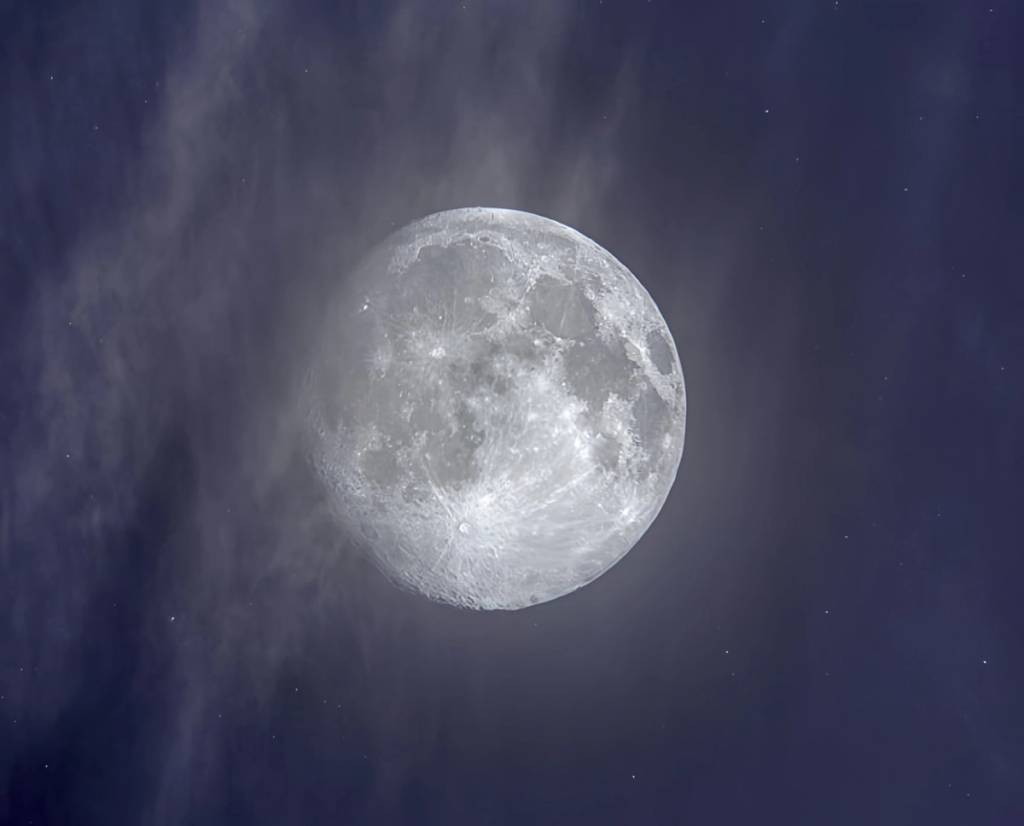 Bright full moon amid wispy clouds in a dark blue night sky.