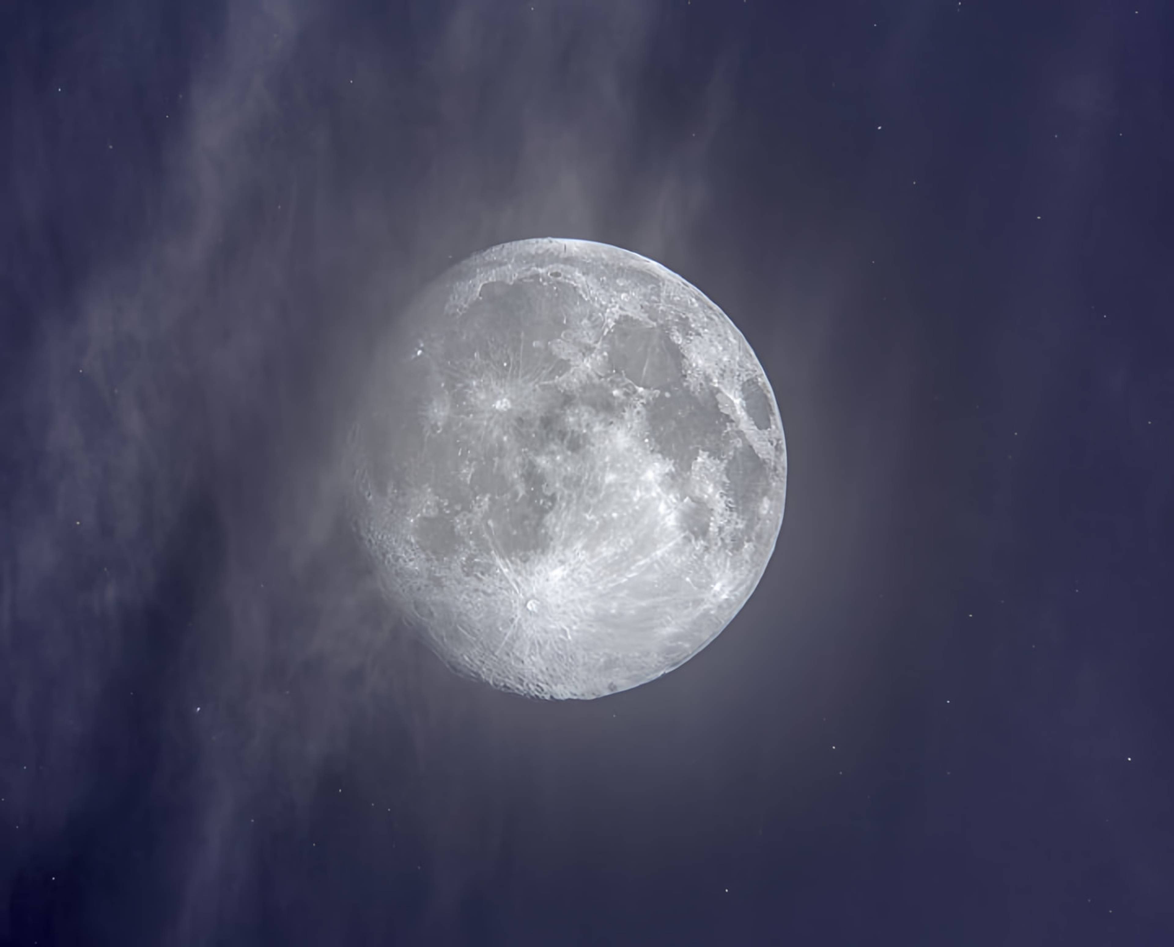 Bright full moon amid wispy clouds in a dark blue night sky.