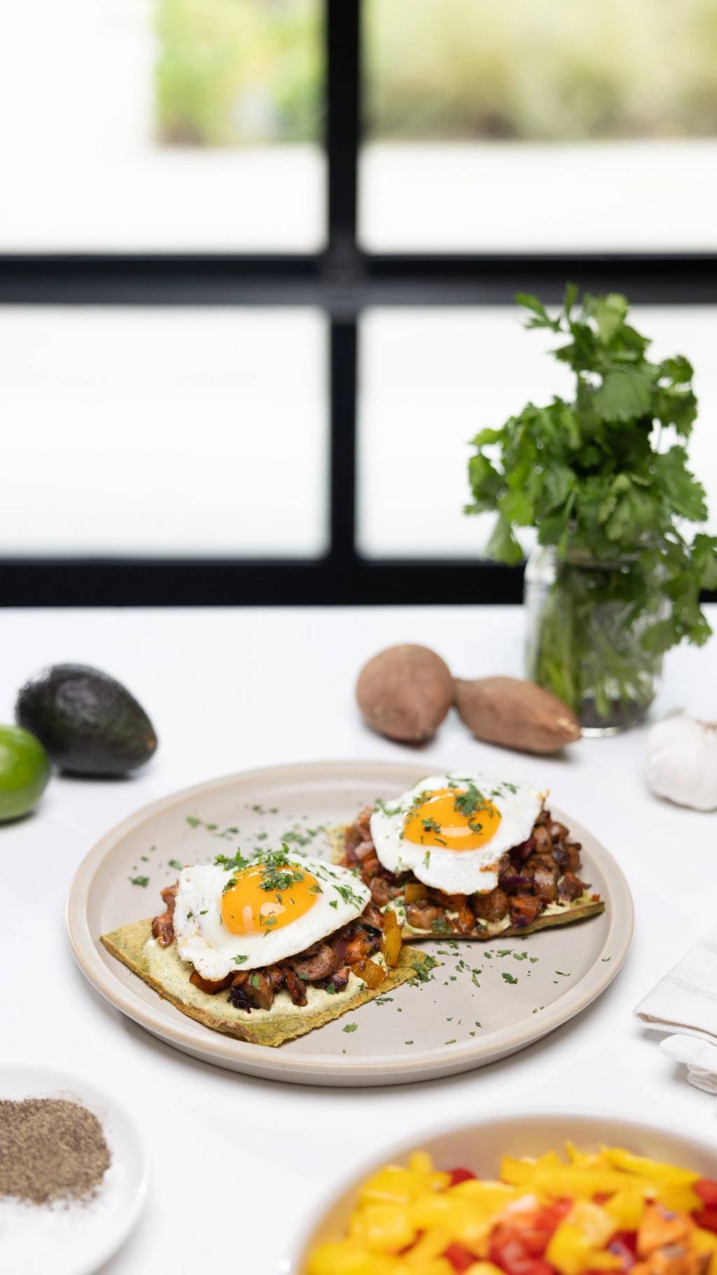 Two breakfast flatbreads topped with sautéed vegetables, fried eggs, and chopped herbs on a plate.