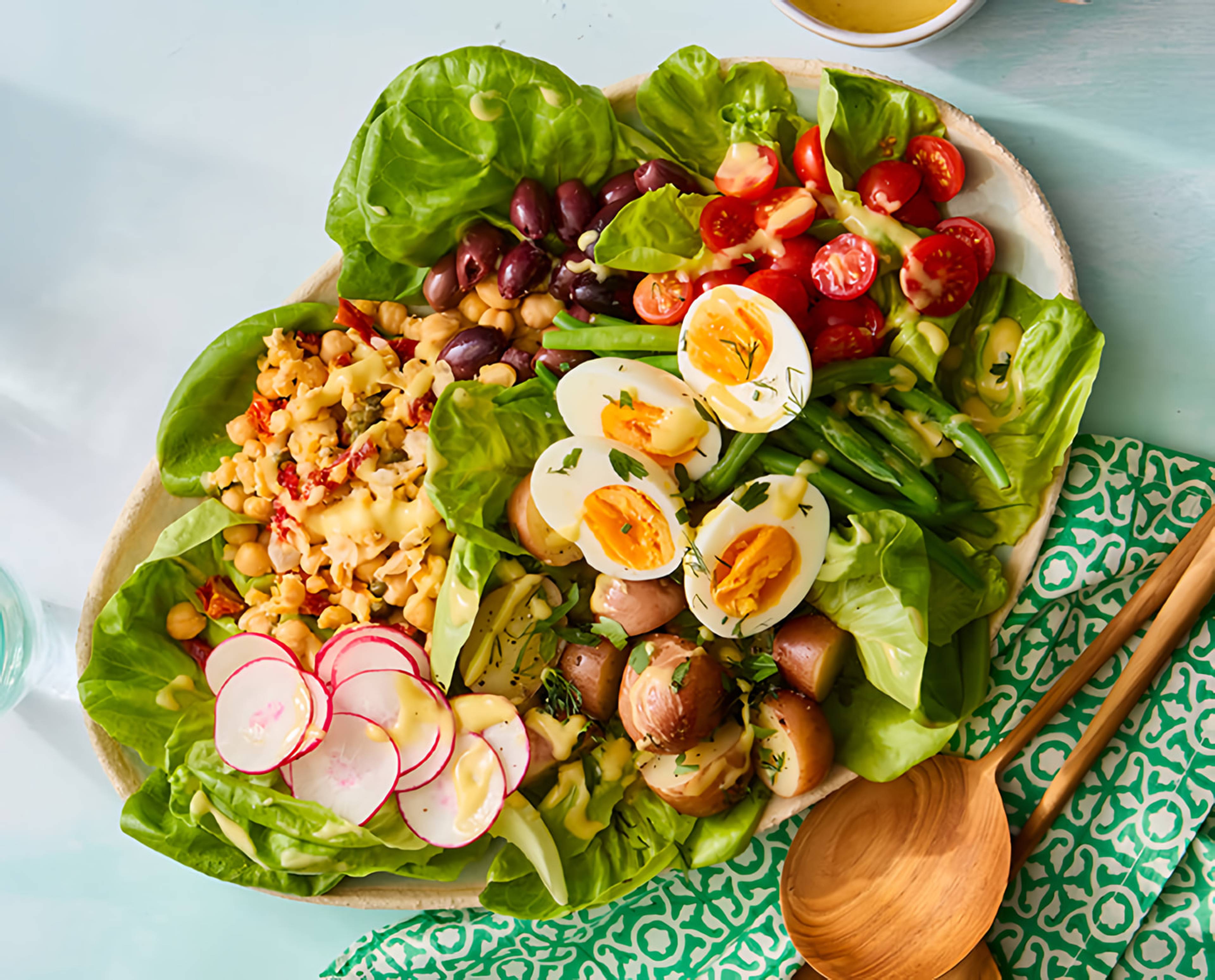 Platter of Niçoise-style salad with lettuce, eggs, green beans, tomatoes, olives, potatoes, and radishes.