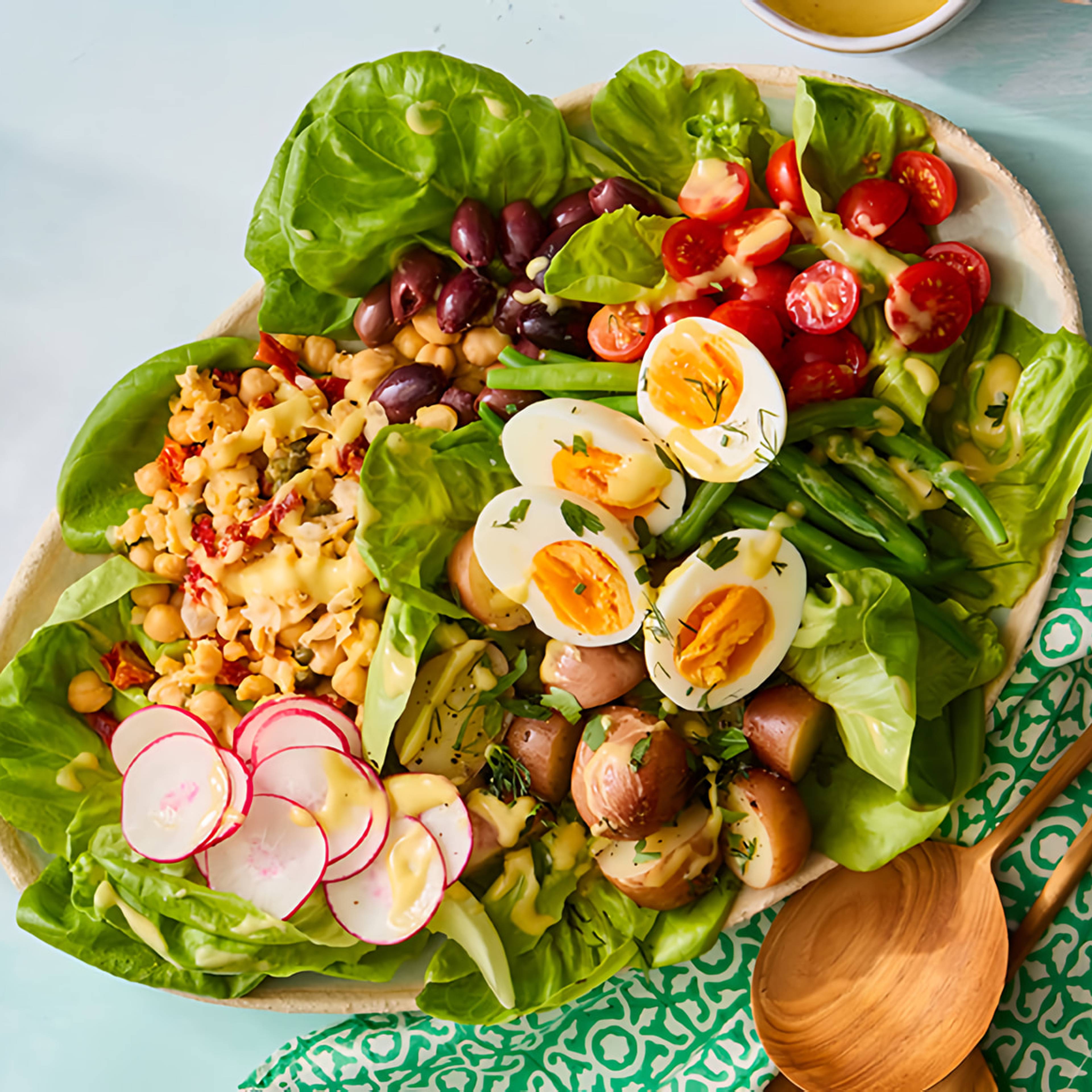 Platter of Niçoise-style salad with lettuce, eggs, green beans, tomatoes, olives, potatoes, and radishes.
