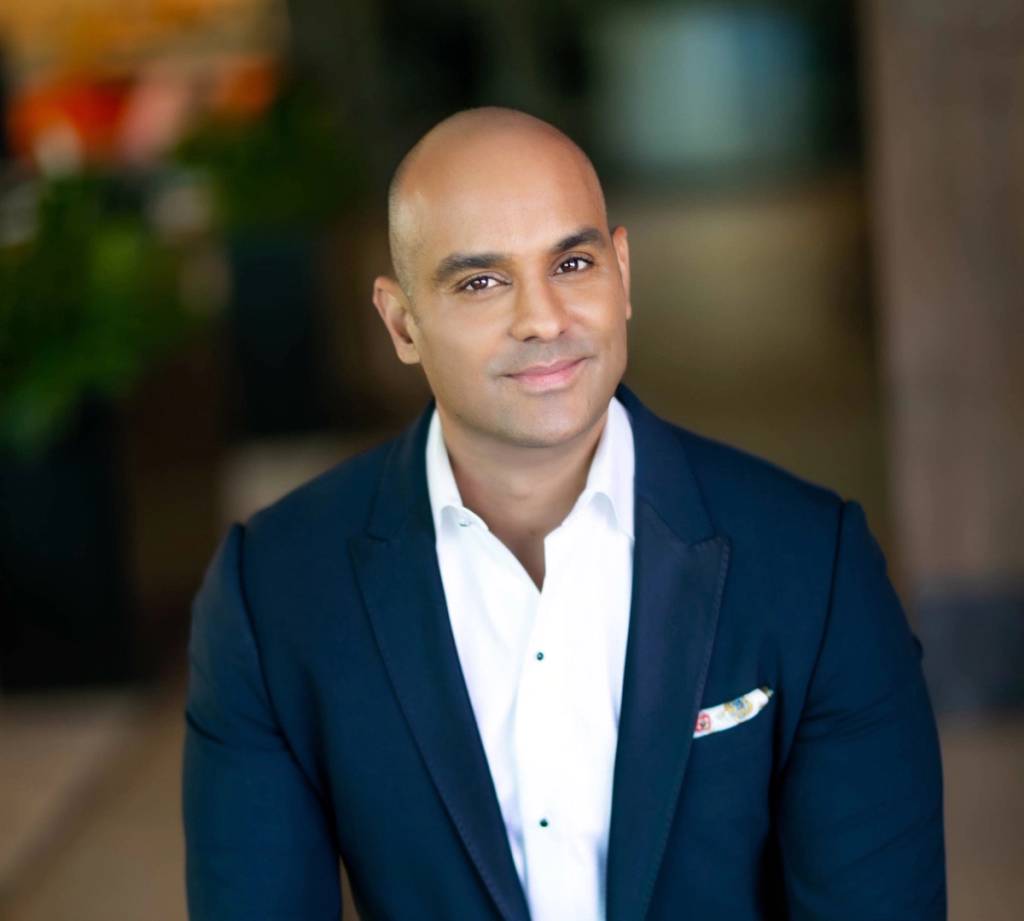 Smiling bald man in a navy suit jacket and white shirt indoors.