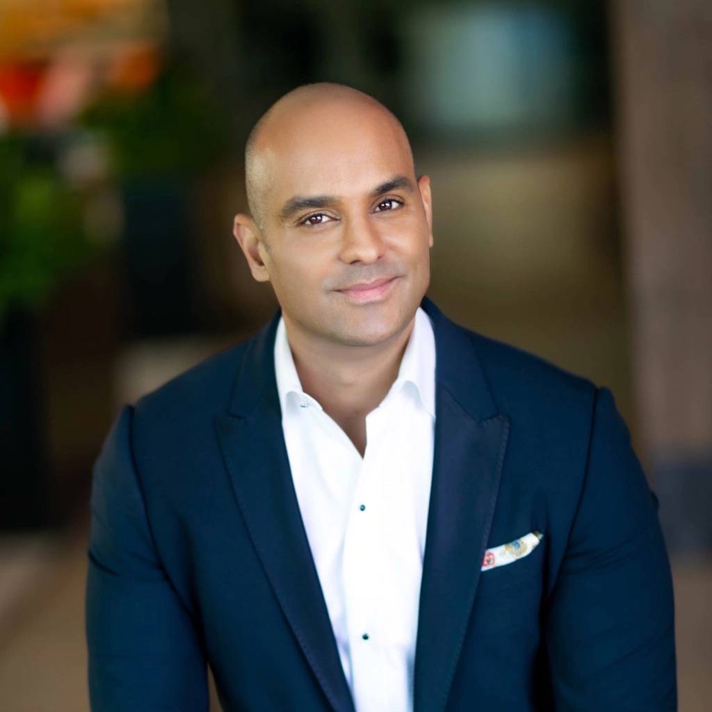 Smiling bald man in a navy suit jacket and white shirt indoors.