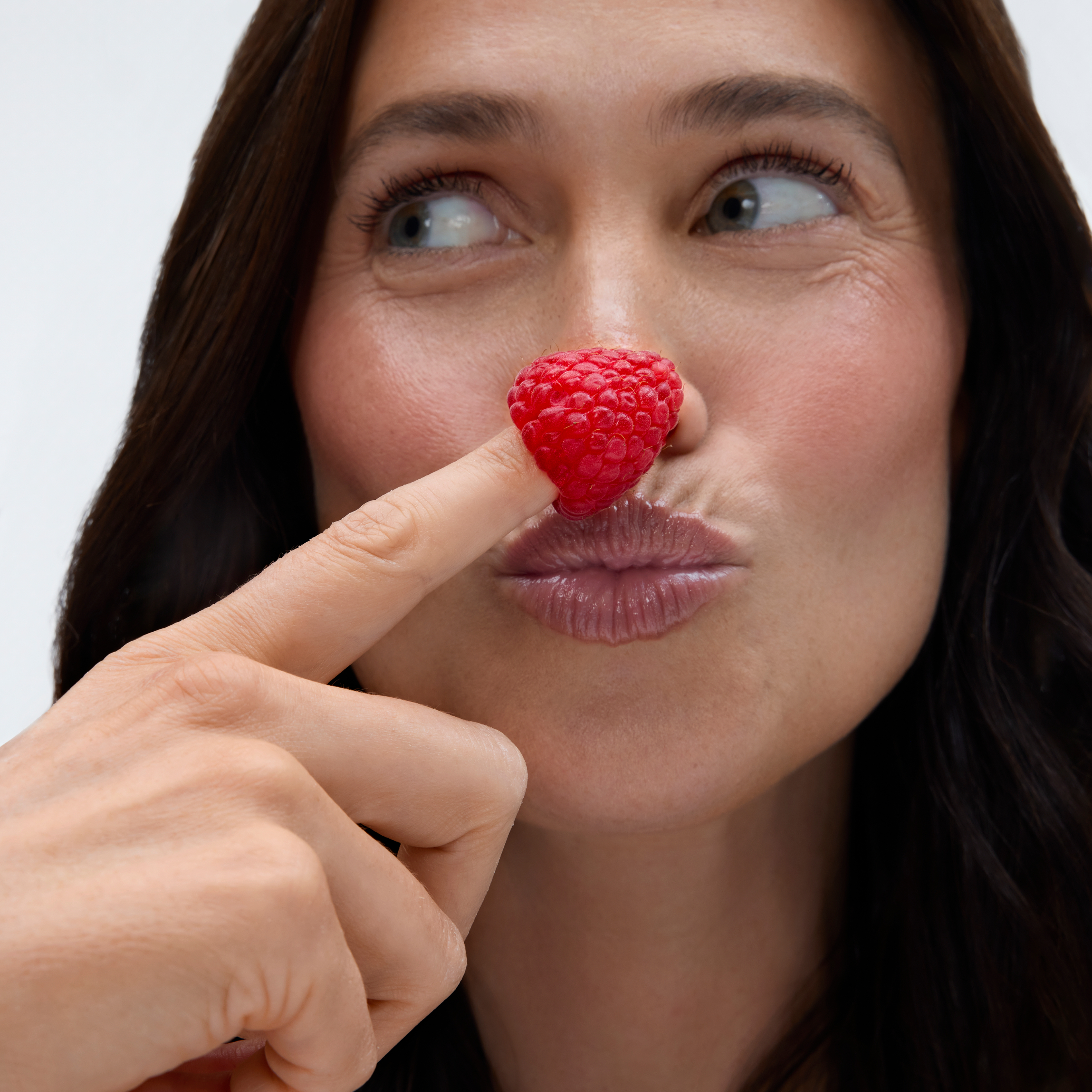 Close-up of a woman touching a raspberry to her nose, looking upward.