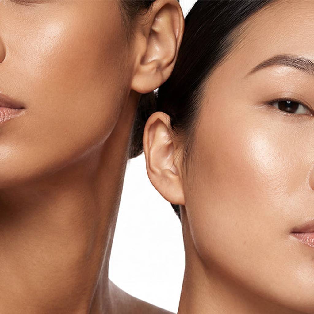 Close-up studio portrait of two women with luminous skin against a white background.