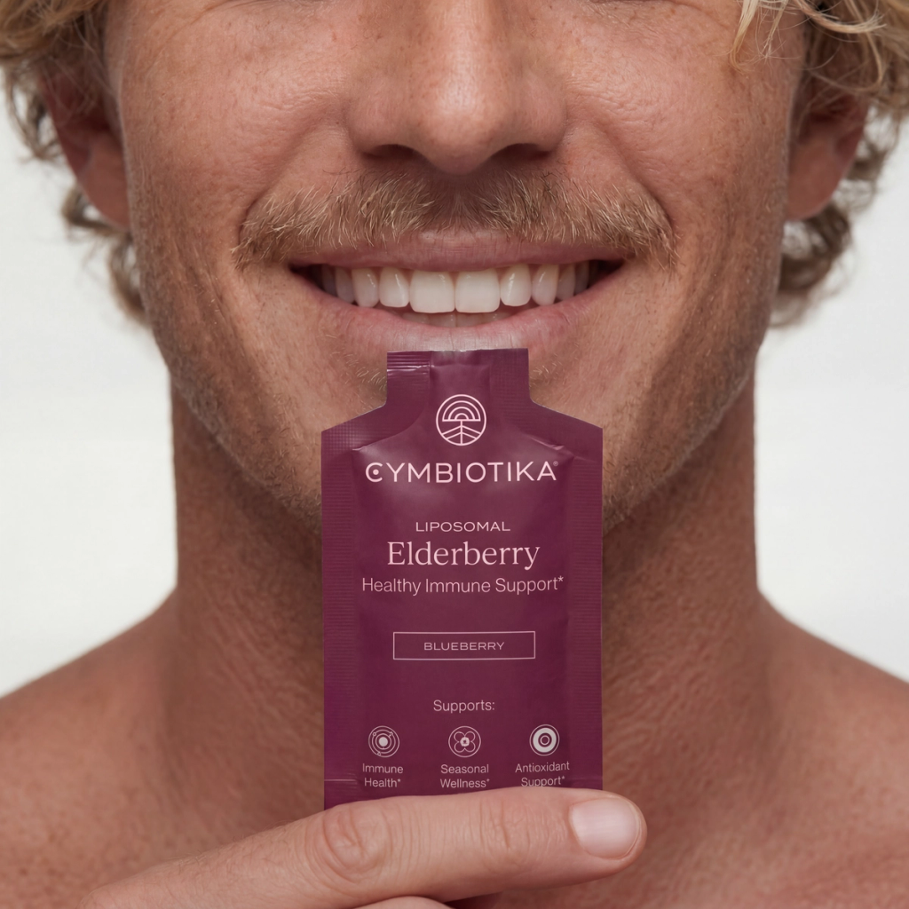 Smiling man holds a Cymbiotika Liposomal Elderberry packet just below his mouth.