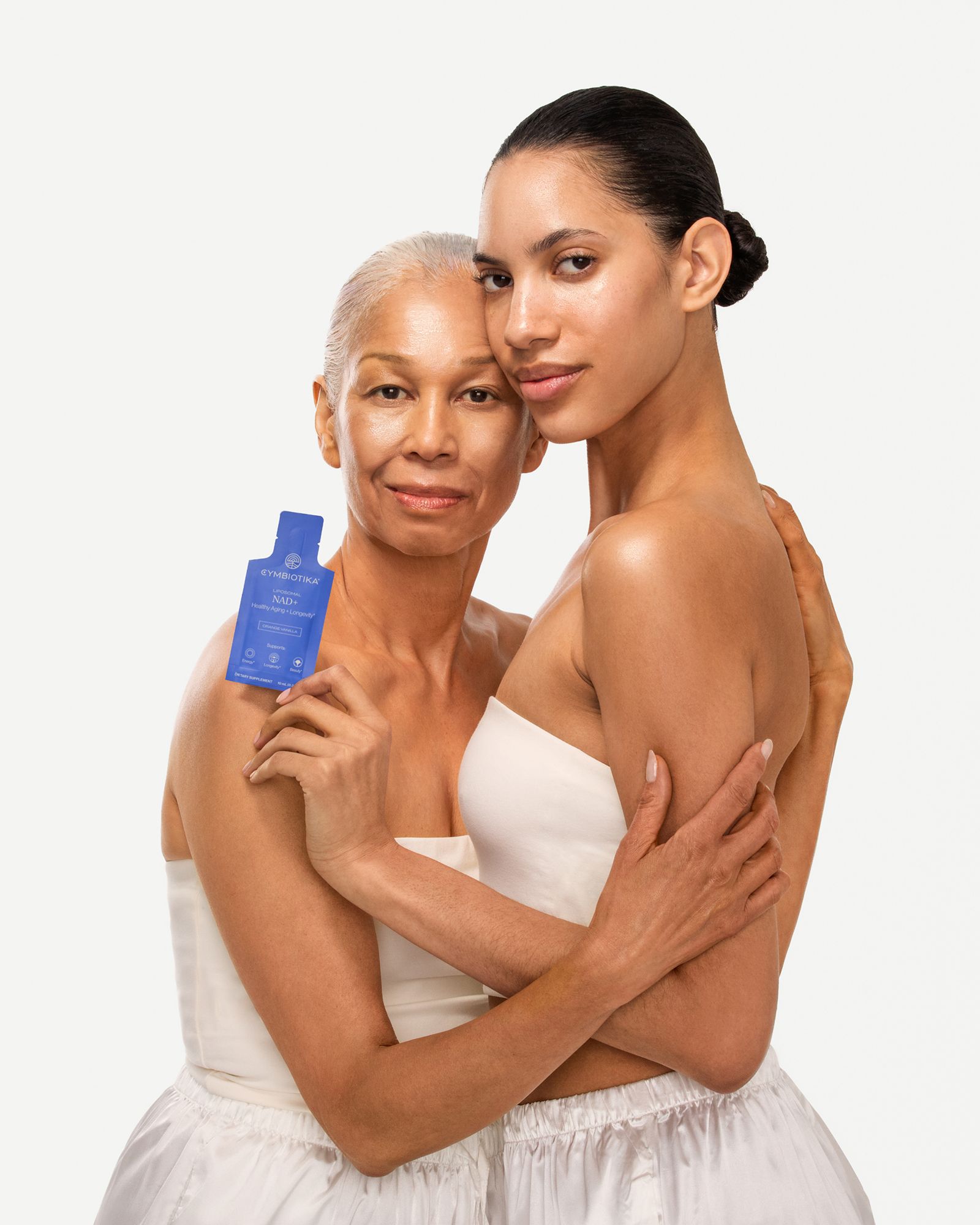 Two women embrace, one holding a blue sachet labeled “NAD+.”