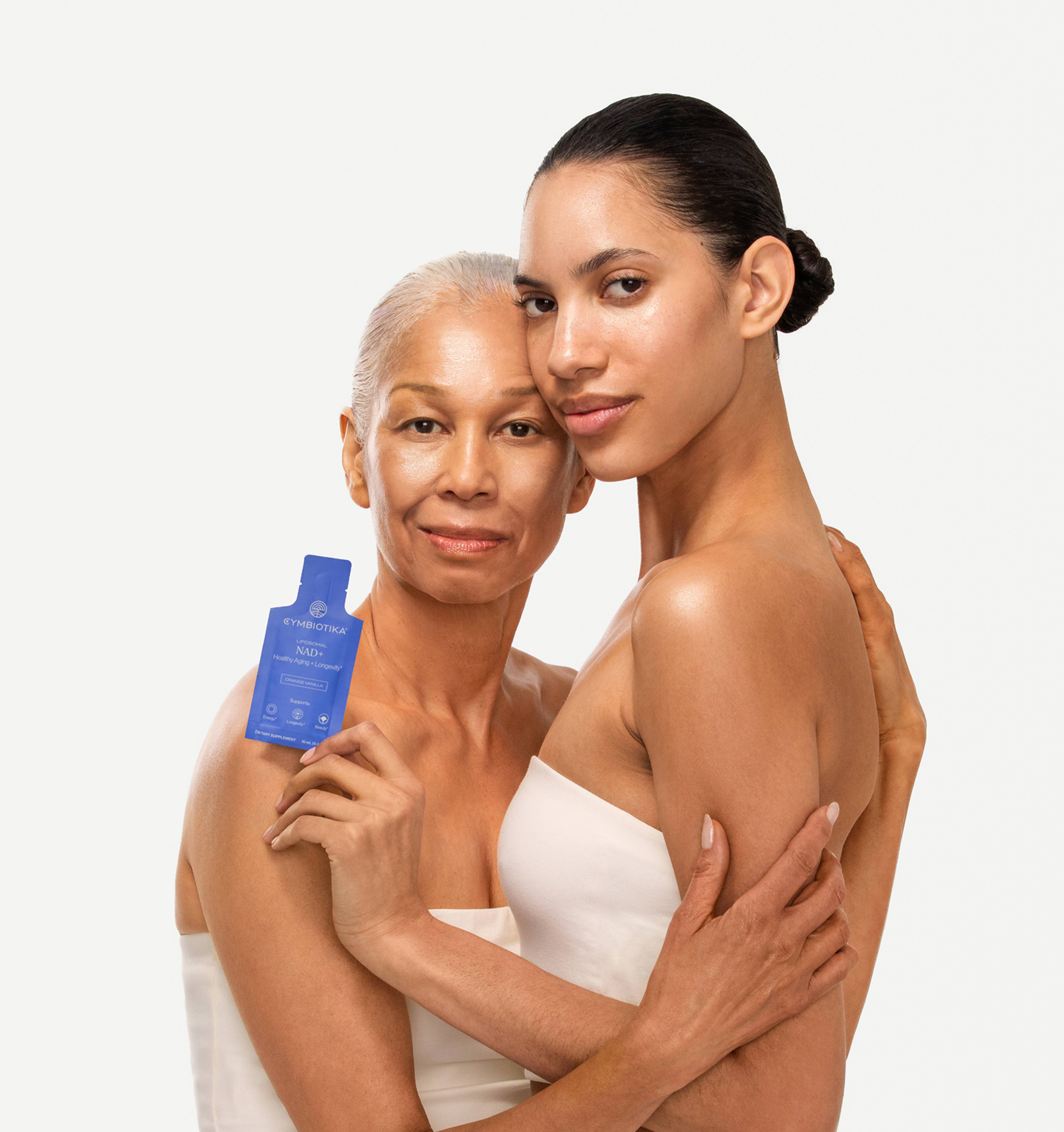 Two women embrace, one holding a blue sachet labeled “NAD+.”