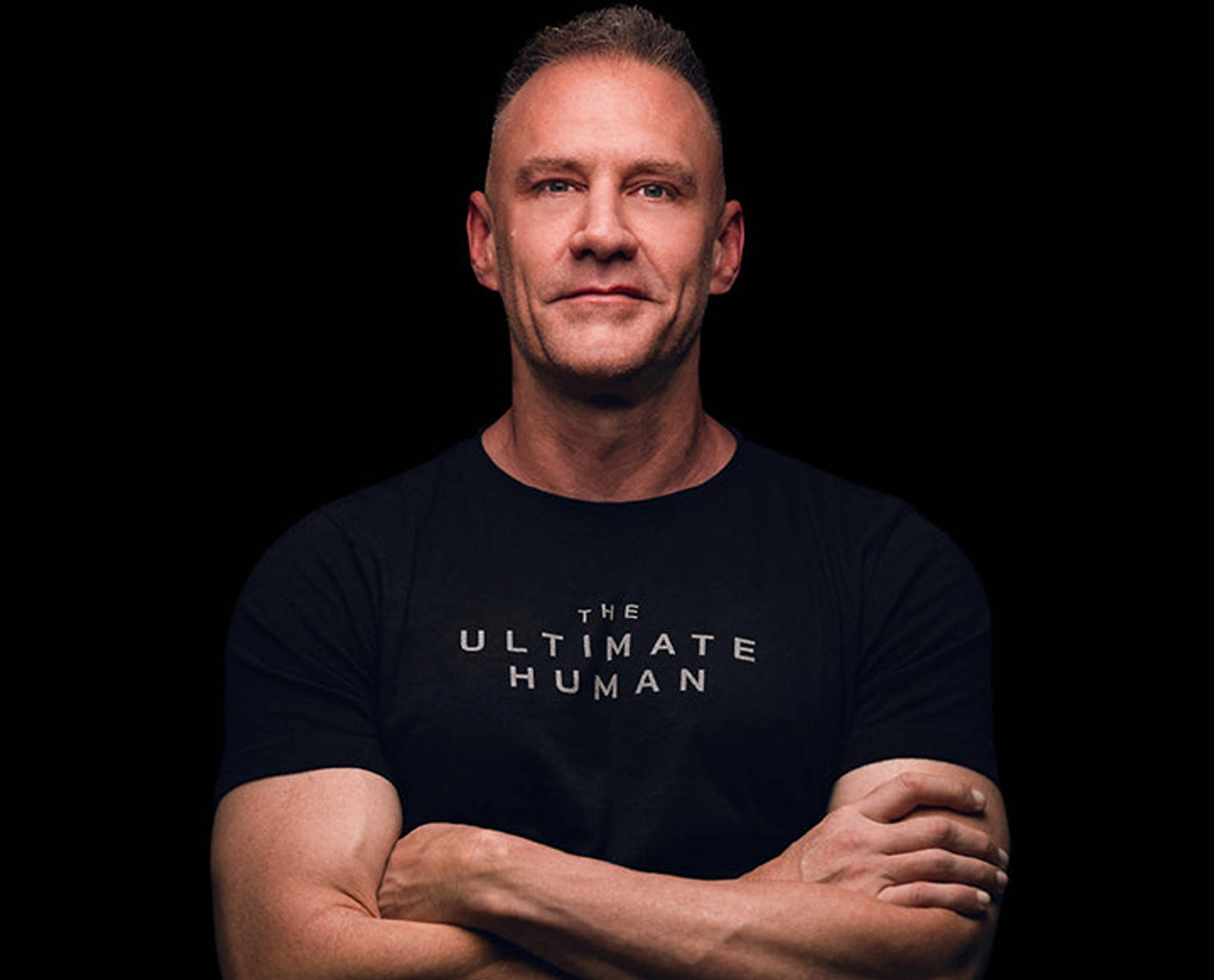 A man stands with his arms crossed, wearing a dark T-shirt.