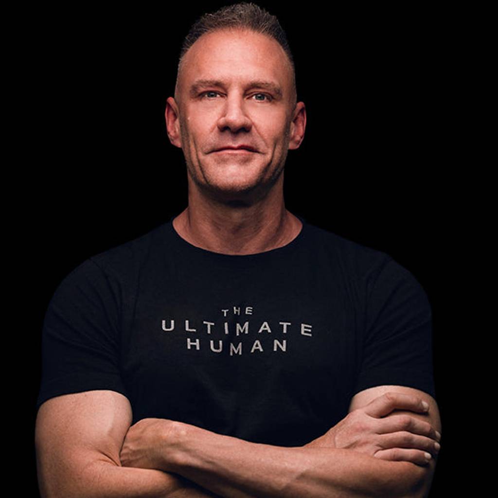A man stands with his arms crossed, wearing a dark T-shirt.