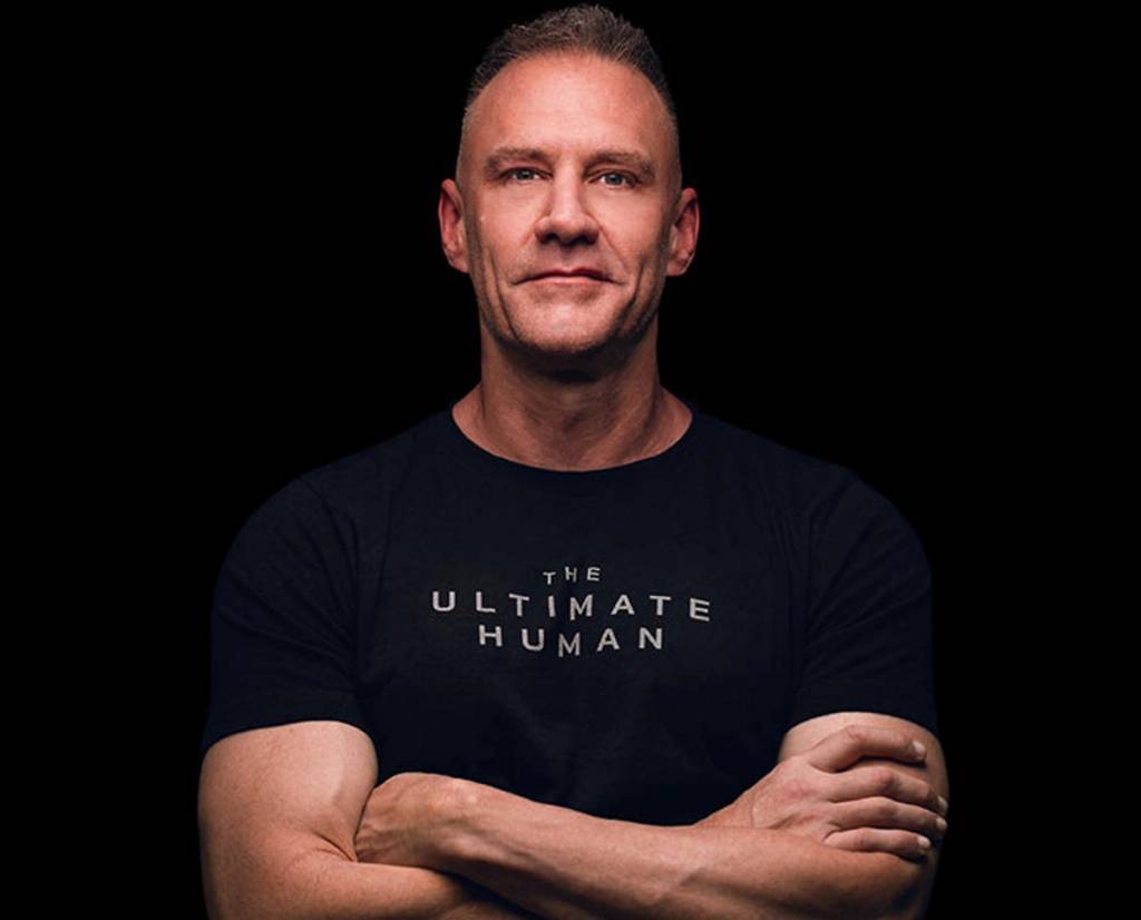 A man stands with his arms crossed, wearing a dark T-shirt.