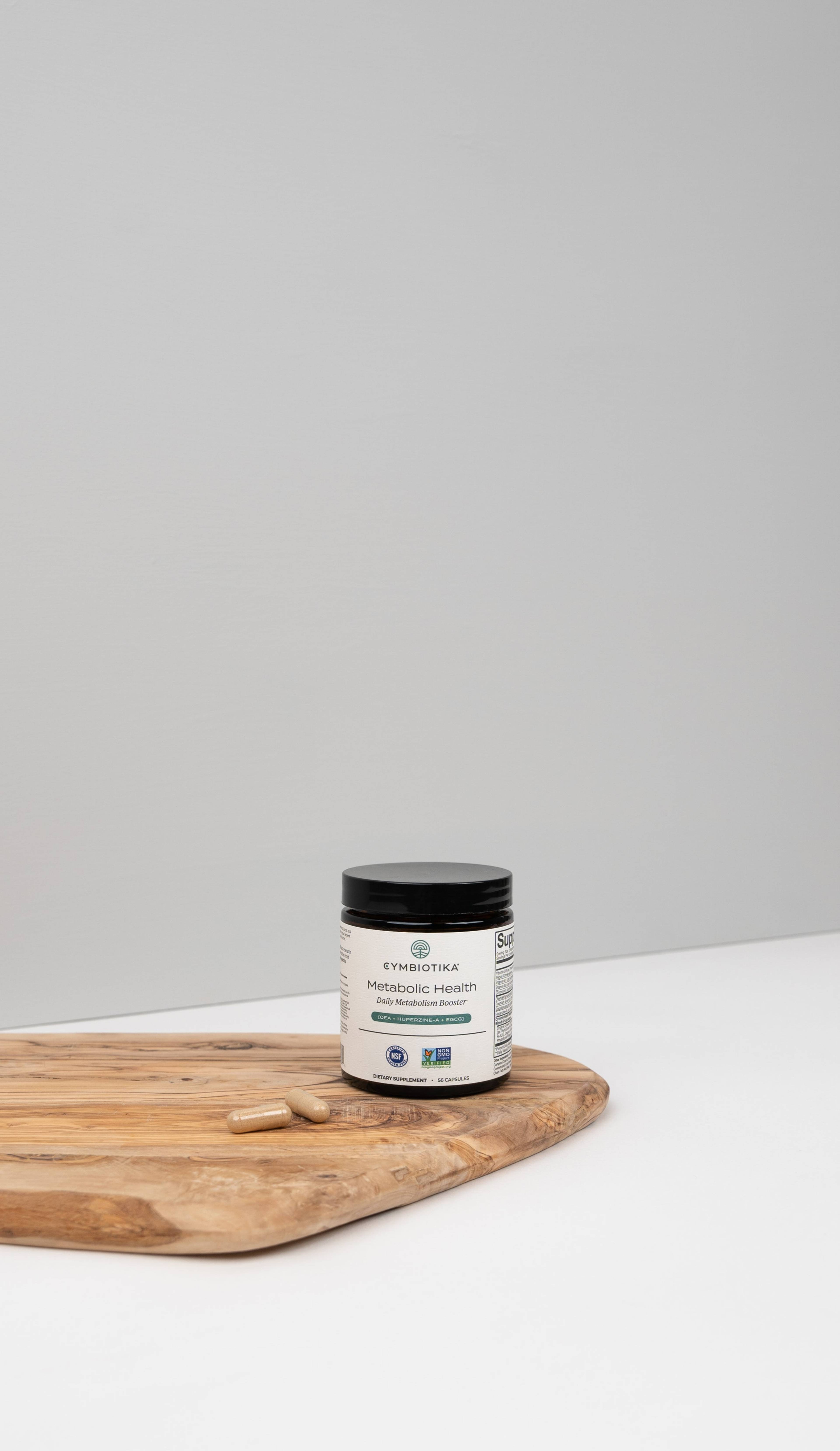 Cymbiotika Metabolic Health supplement jar on a wooden board with two capsules.