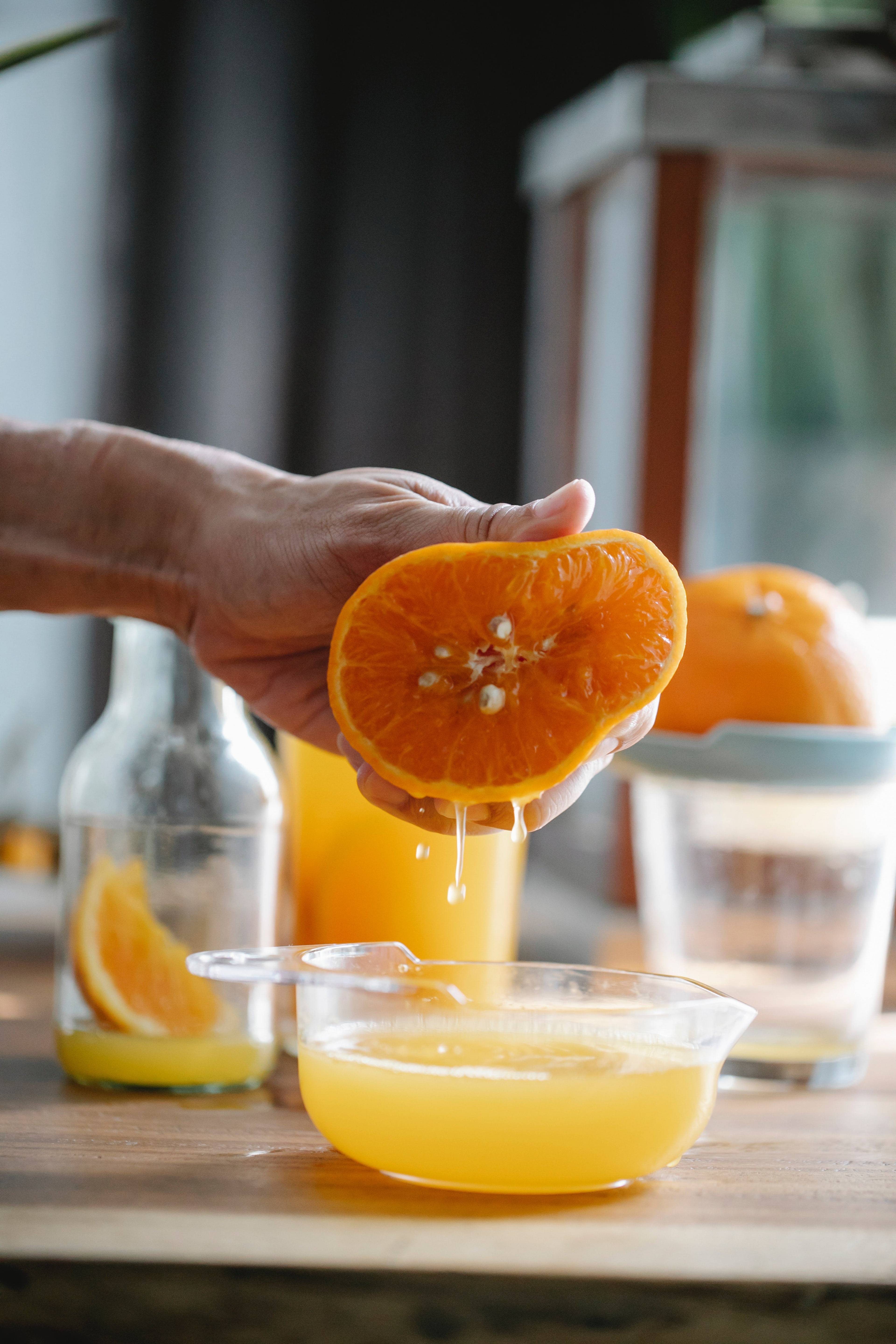 Hand squeezing a halved orange over a glass bowl of fresh juice on a kitchen counter.