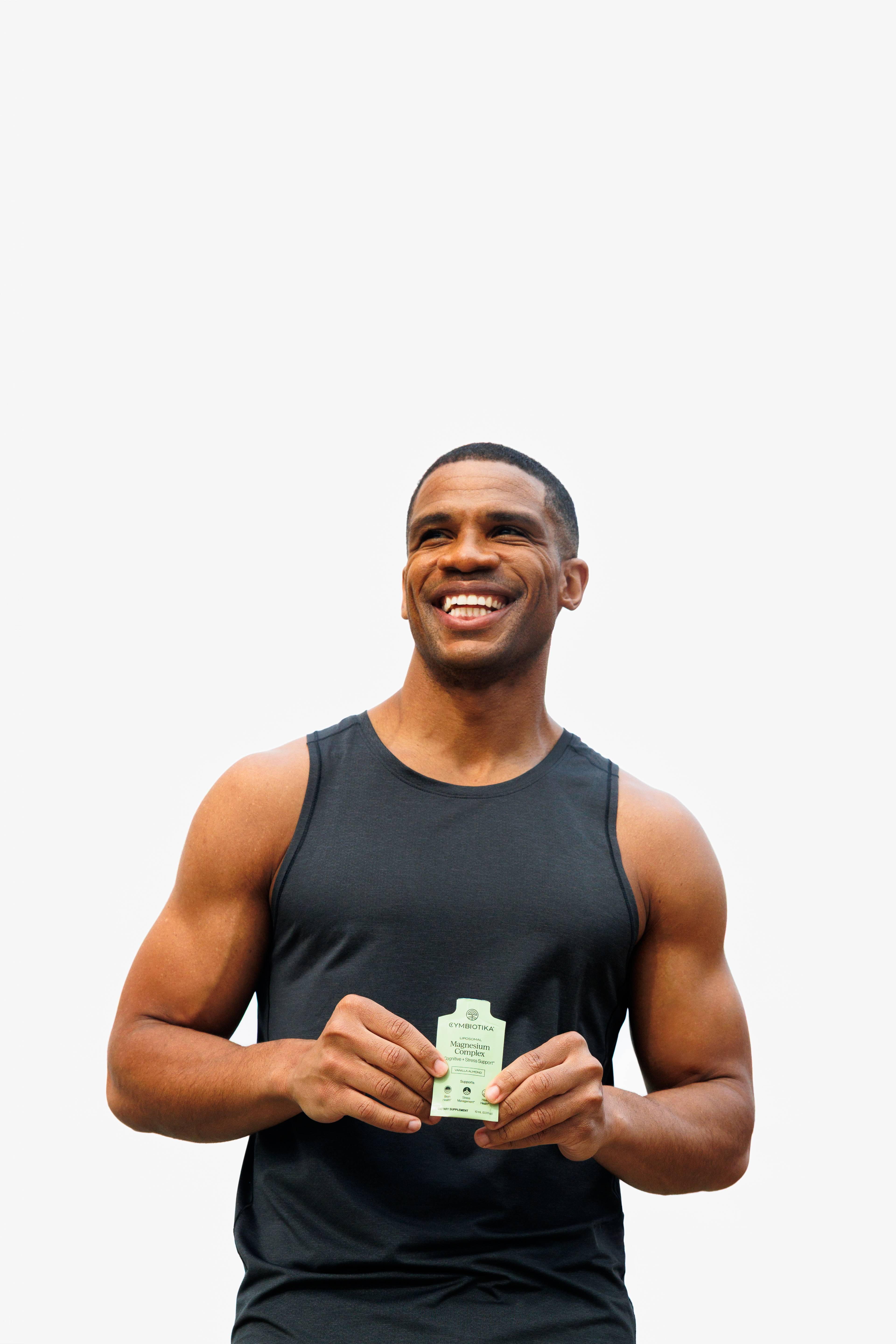 Smiling man in a black tank top holding a small Magnesium Complex packet.