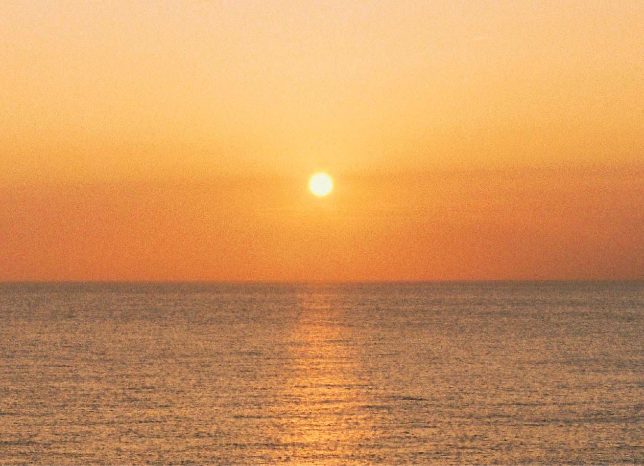 A low sun above a calm ocean, casting a golden reflection across the water.