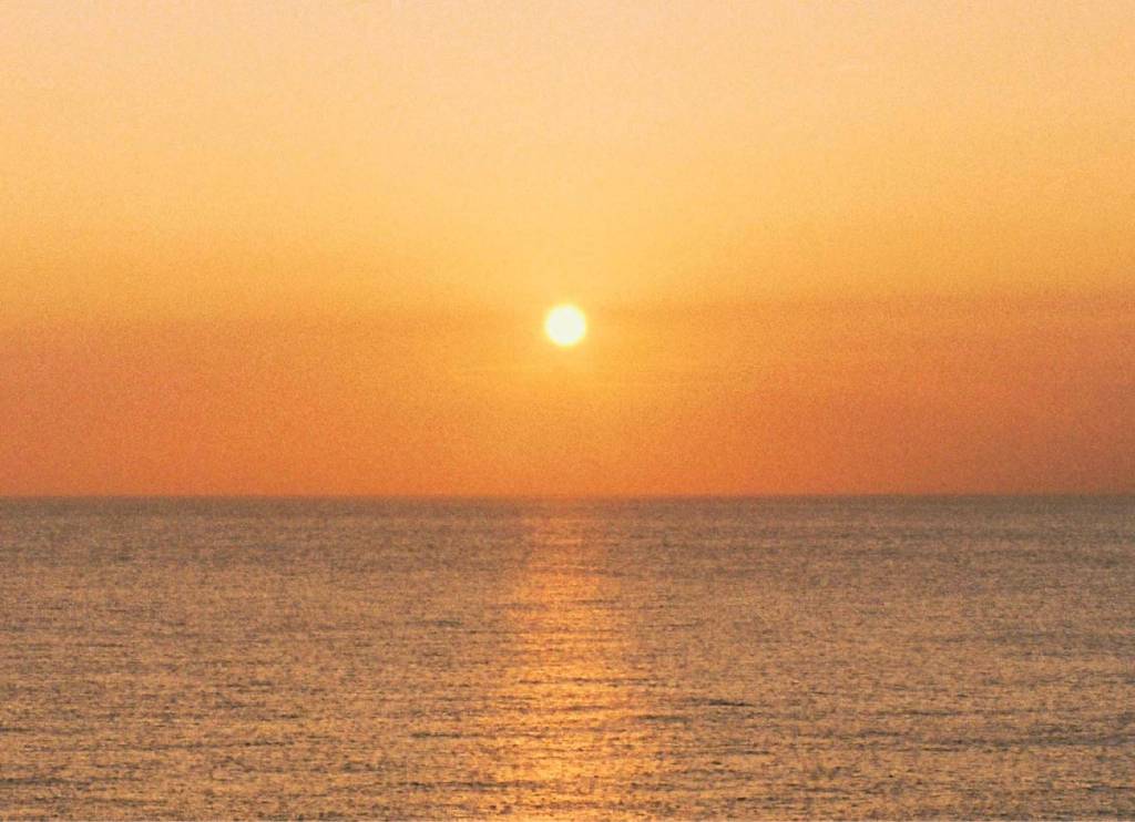 A low sun above a calm ocean, casting a golden reflection across the water.