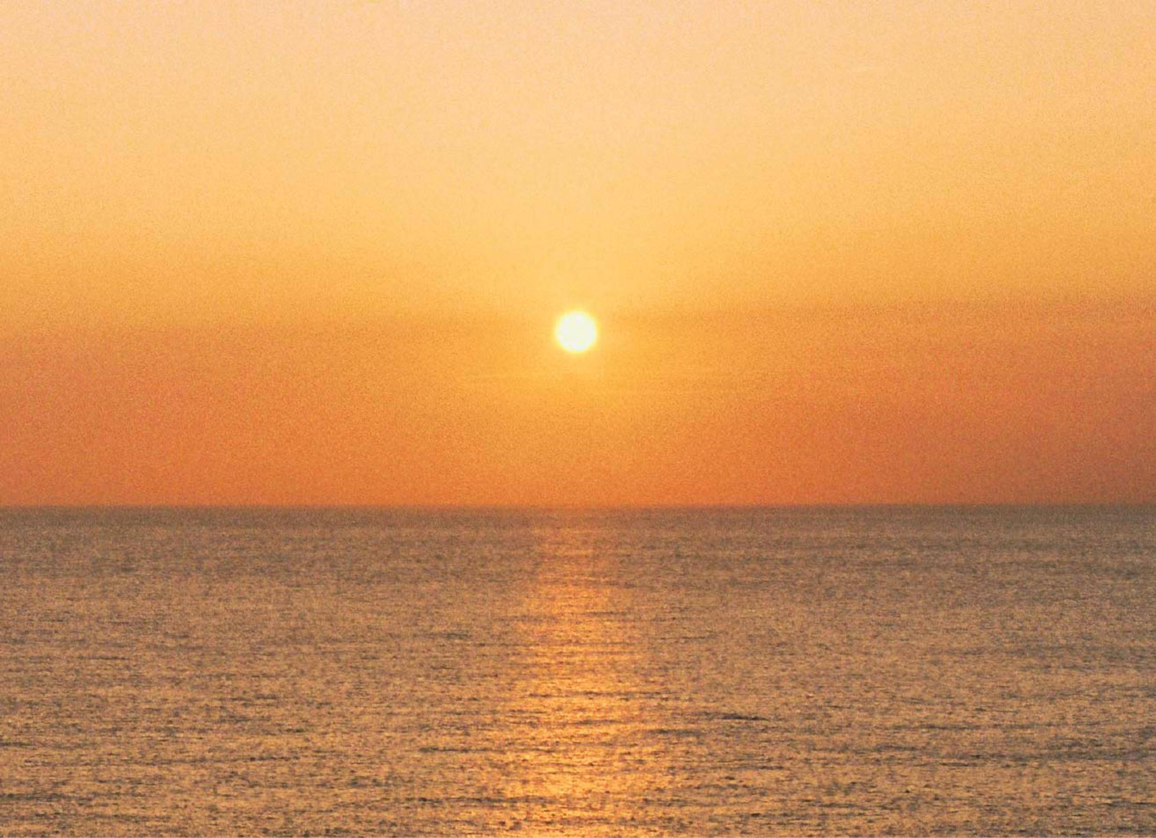 A low sun above a calm ocean, casting a golden reflection across the water.