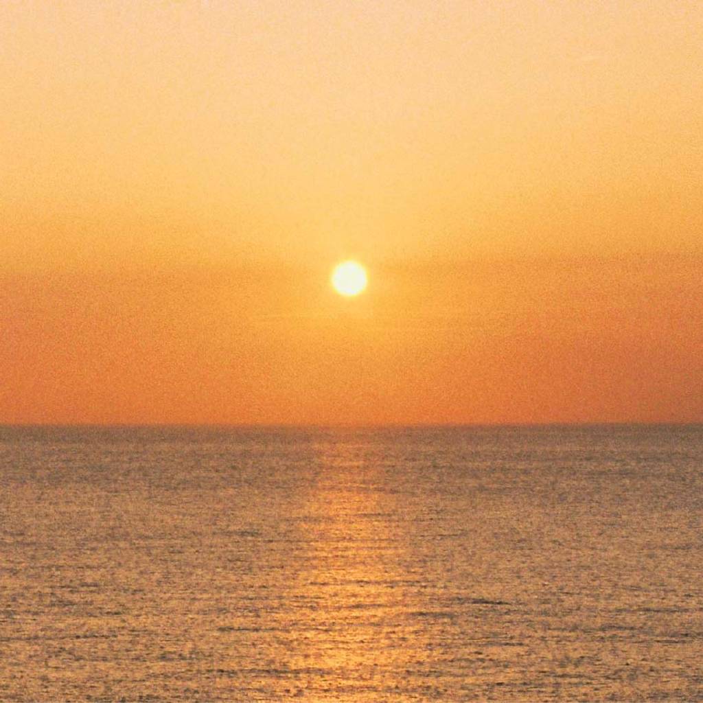 A low sun above a calm ocean, casting a golden reflection across the water.