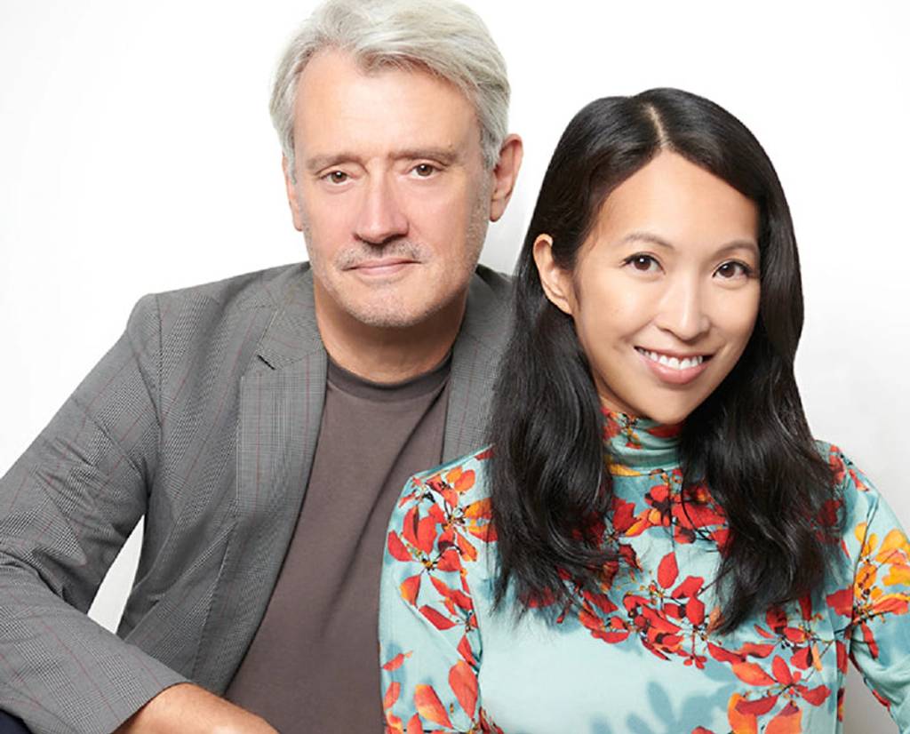 Portrait of a gray-haired man in a gray blazer beside a smiling woman in a floral turquoise top.