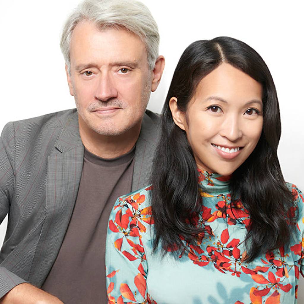 Portrait of a gray-haired man in a gray blazer beside a smiling woman in a floral turquoise top.