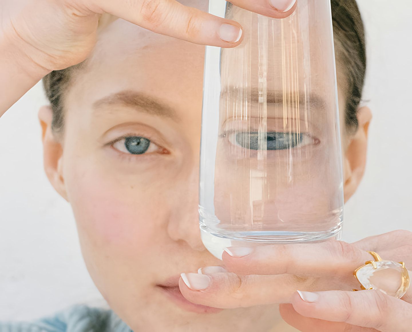 Close-up of a woman holding a clear glass of water in front of one eye.
