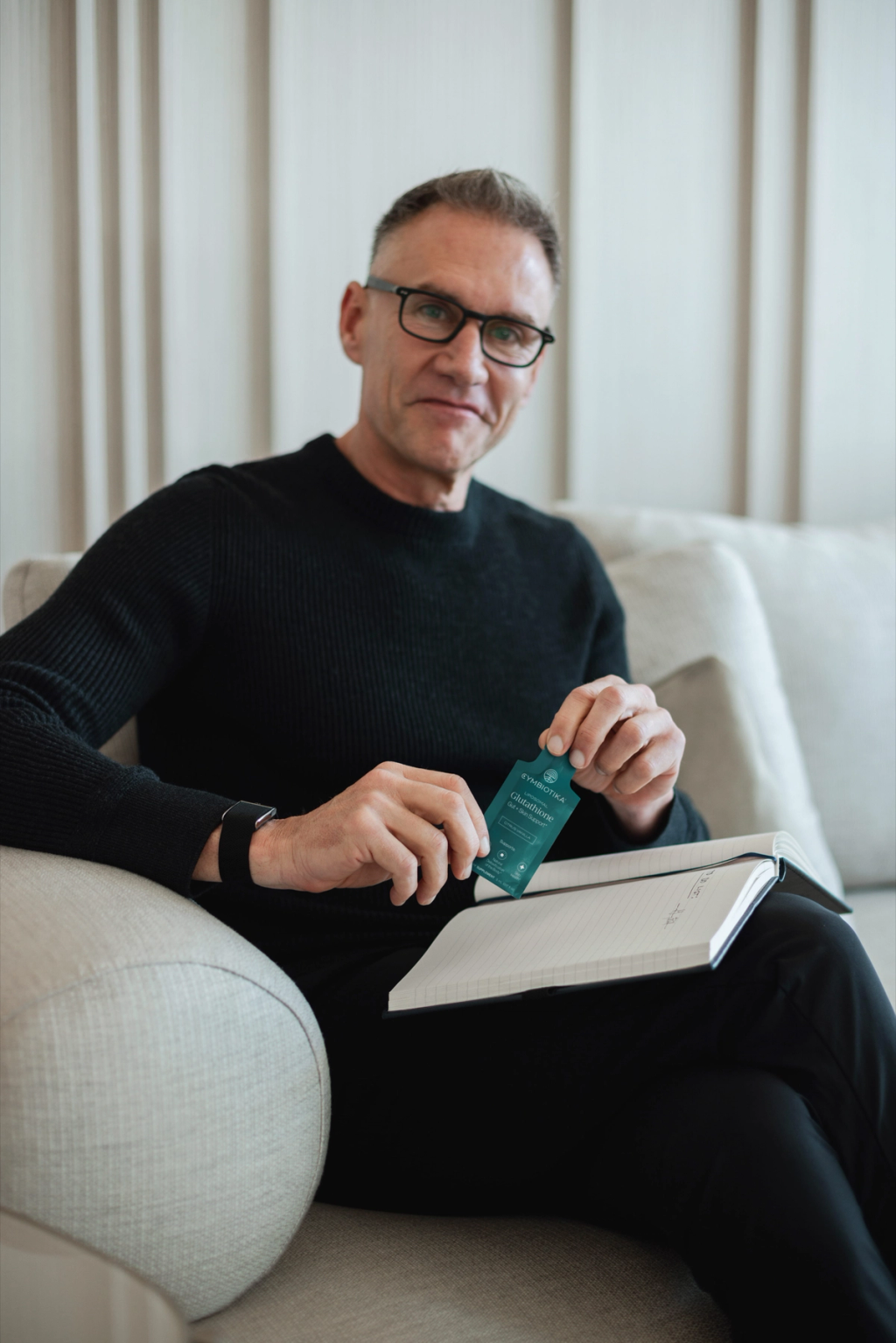 Man seated with an open notebook, holding a teal supplement packet.